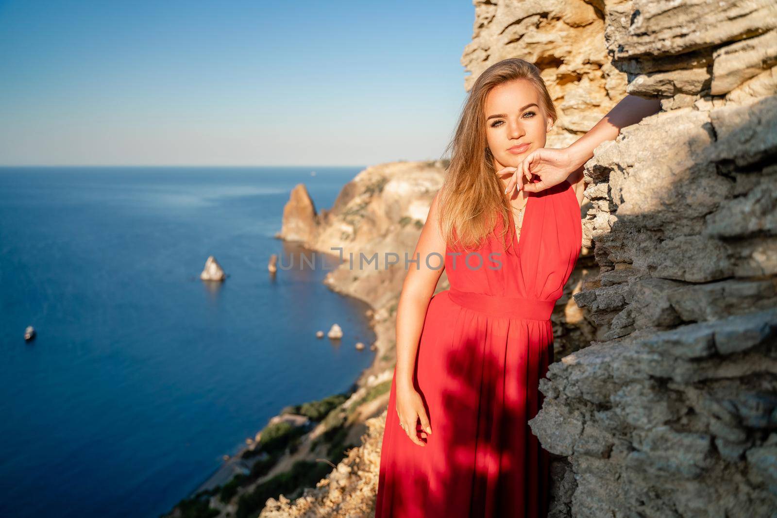 A woman in a red flying dress fluttering in the wind, against the backdrop of the sea