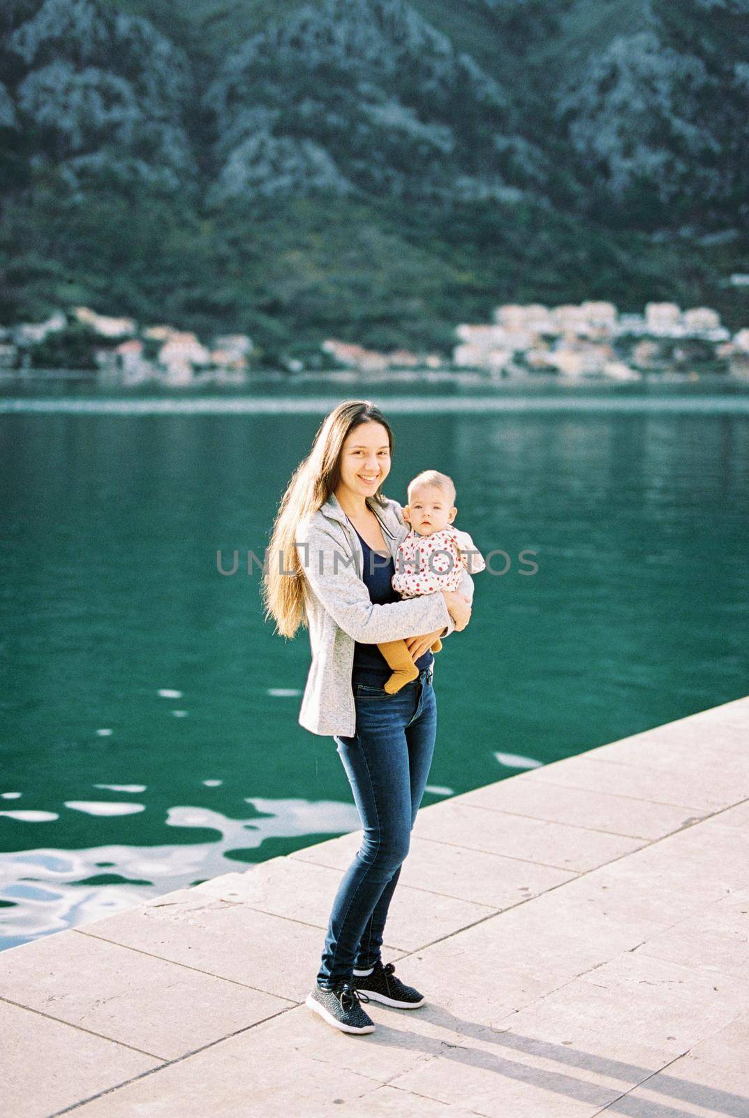 Mom with a baby in her arms stands on the pier. High quality photo