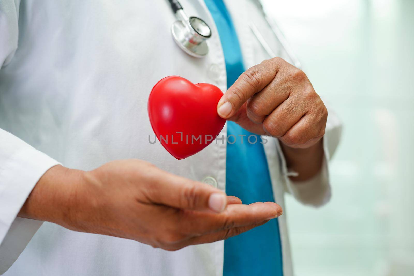Asian woman doctor holding red heart for health in hospital.