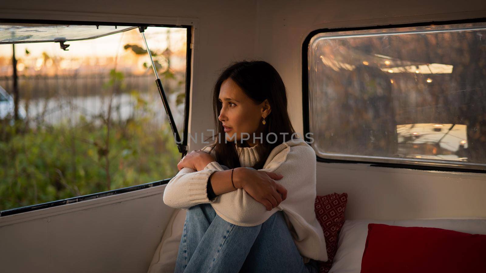 Pensive Caucasian woman in light sweater motorhome in warm autumn. Travel in a van