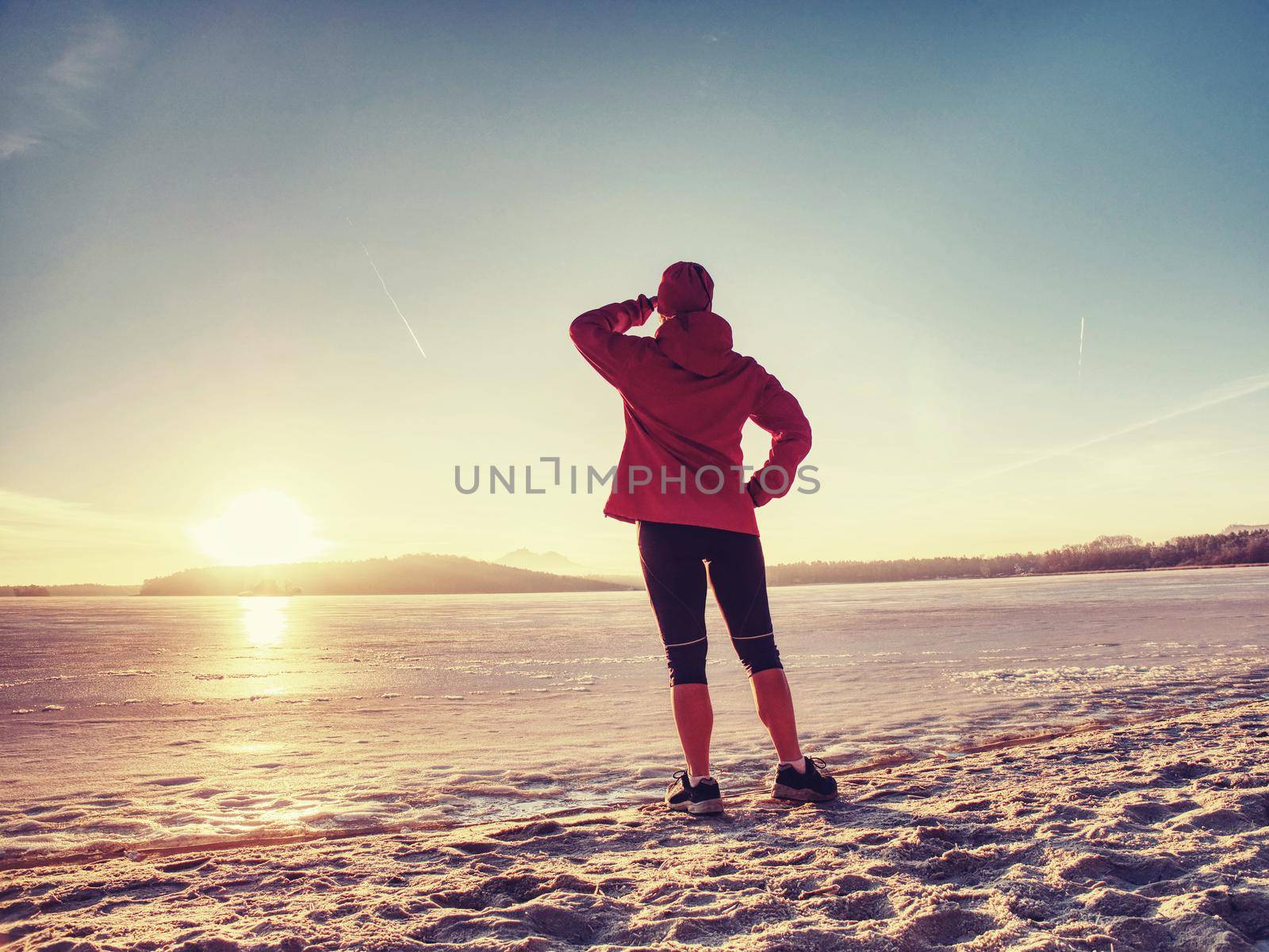 Caucasian girl with slim fit body doing stretching exercises before jogging workout on winter beach against blurred ocean 