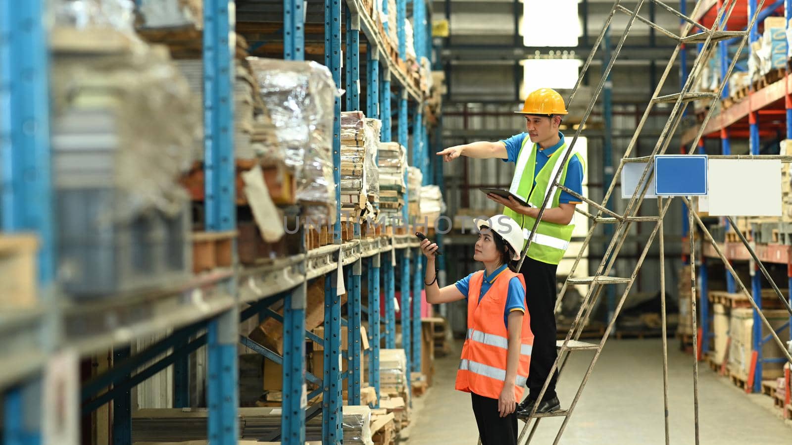 Two young warehouse worker using barcode scanner checking stock on the shelves in a large warehouse.