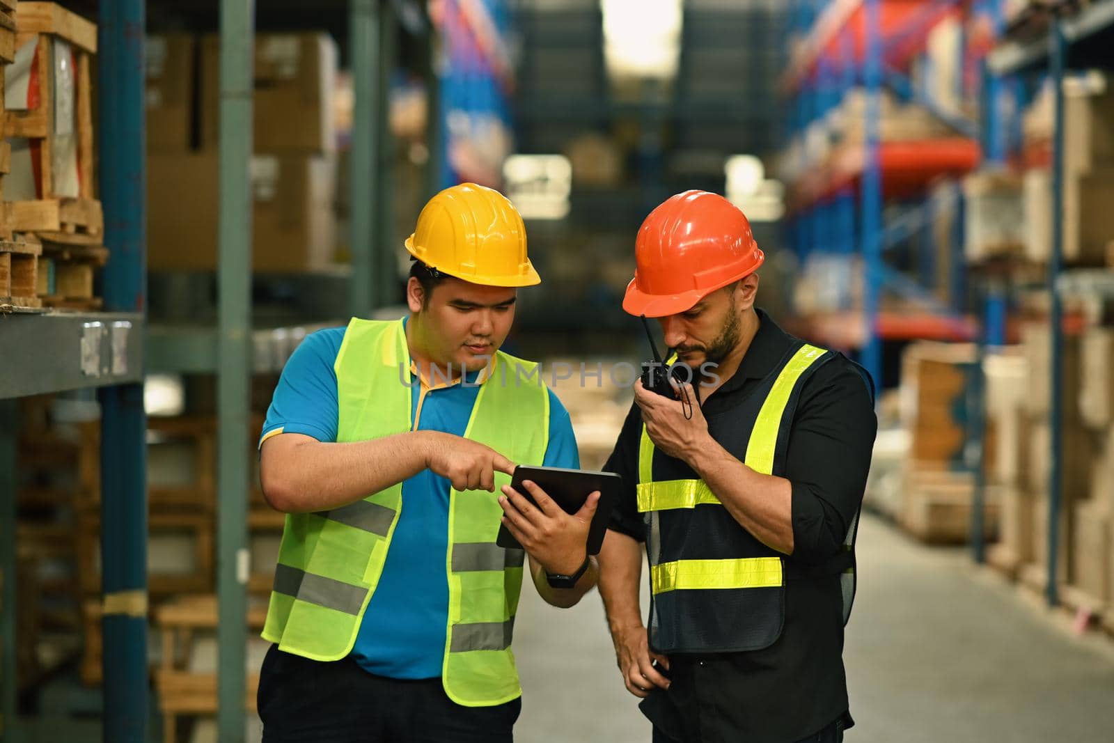 Warehouse managers and worker checking newly arrived goods on digital tablet while standing near tall shelves in large warehouse.