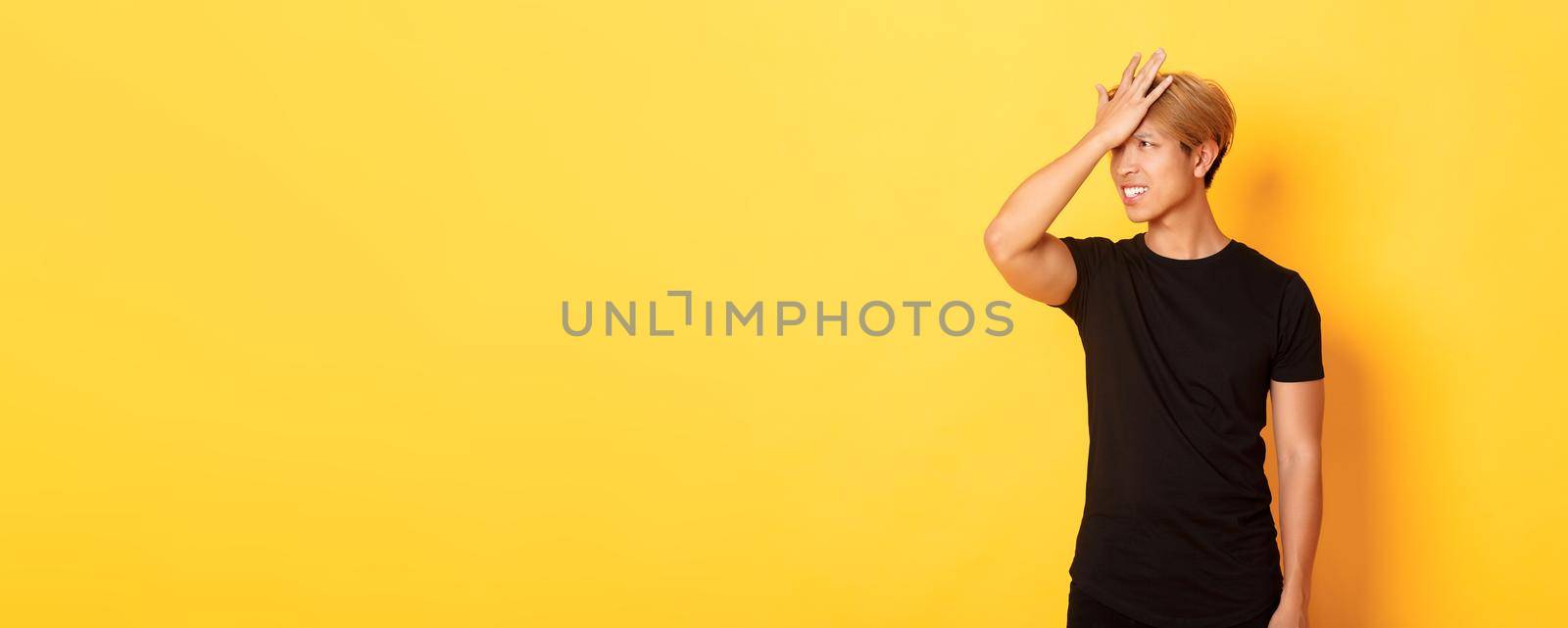 Upset and troubled asian guy snap forehead forgetful, standing over yellow background.