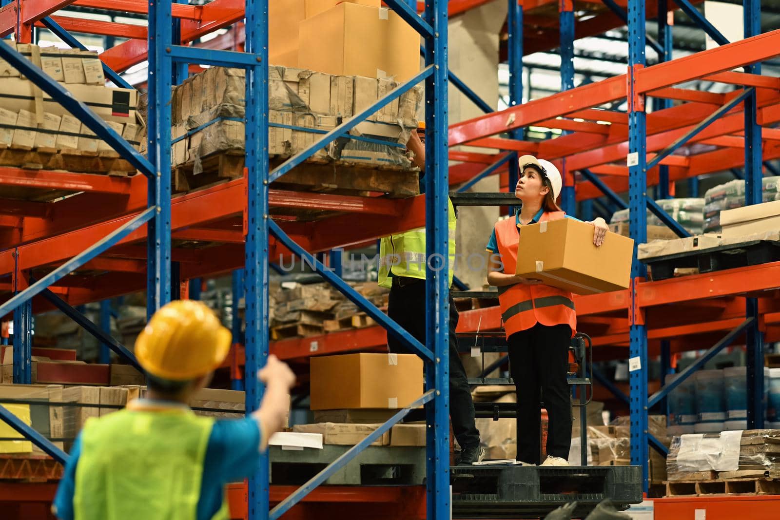 Group of warehouse workers working in a large warehouse between rows of tall shelves full of packed boxes.