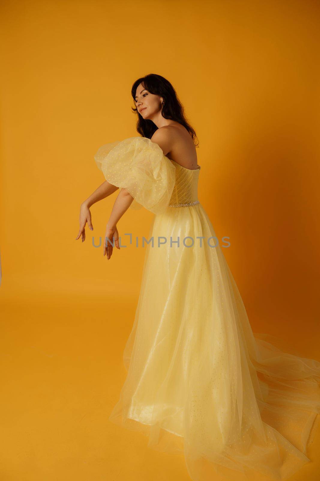 Portrait of a beautiful middle-aged woman in a yellow dress, her hair pulled up against a yellow background by Matiunina