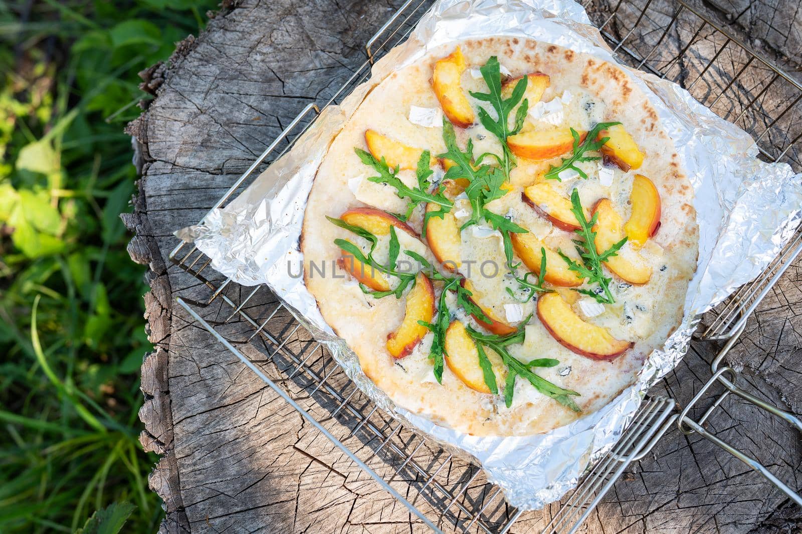 Very tasty and interesting pizza with peach and dor blue with arugula. Delicious, interesting taste of fruit pizza. Grilled pizza, outdoor recreation. by sfinks