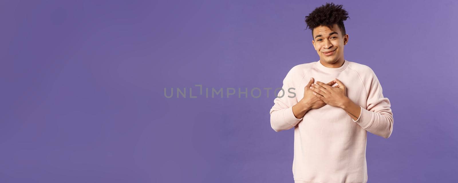 Portrait of touched silly young man left speechless and flattered, sobbing as being hit right into heart with dear warm words and praises, pleased standing purple background.