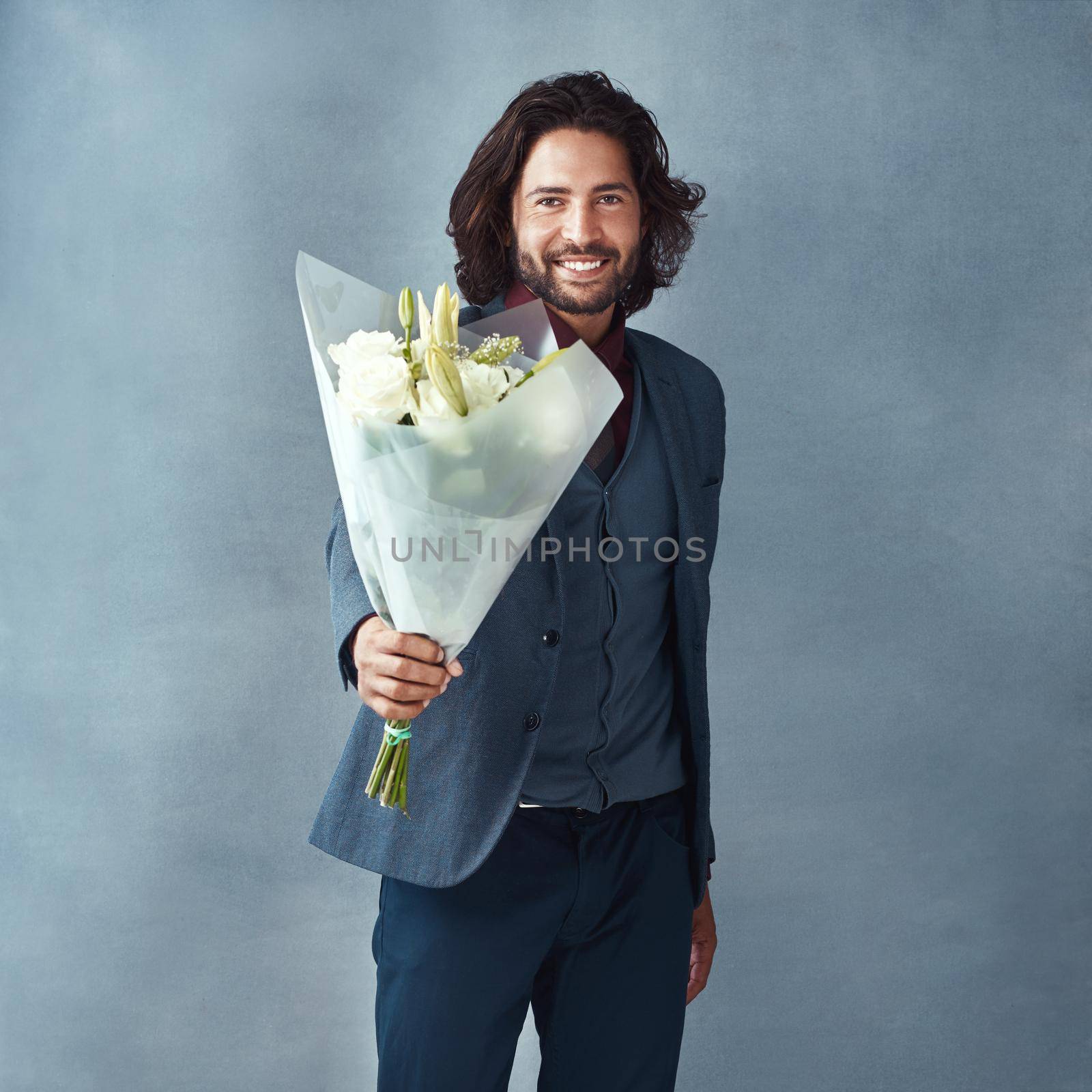 He knows how to turn up the romance. Studio shot of a stylishly dressed handsome young man holding a bouquet of flowers against a gray background