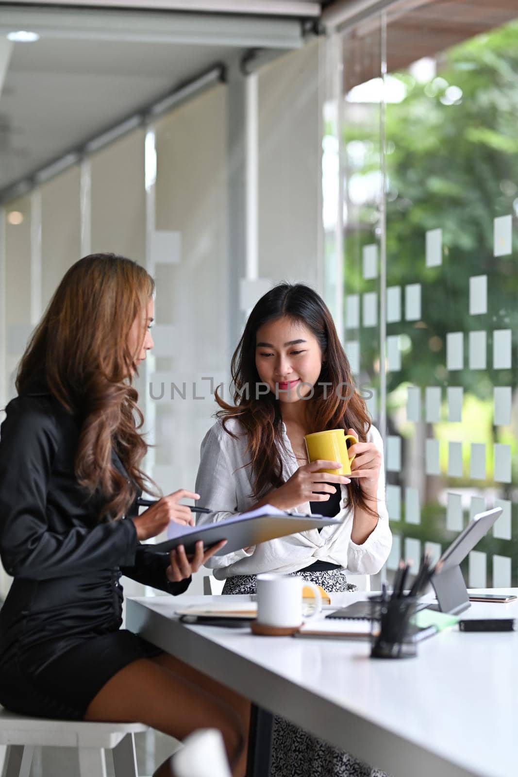 Two smiling businesswoman talking each other during coffee breaking.