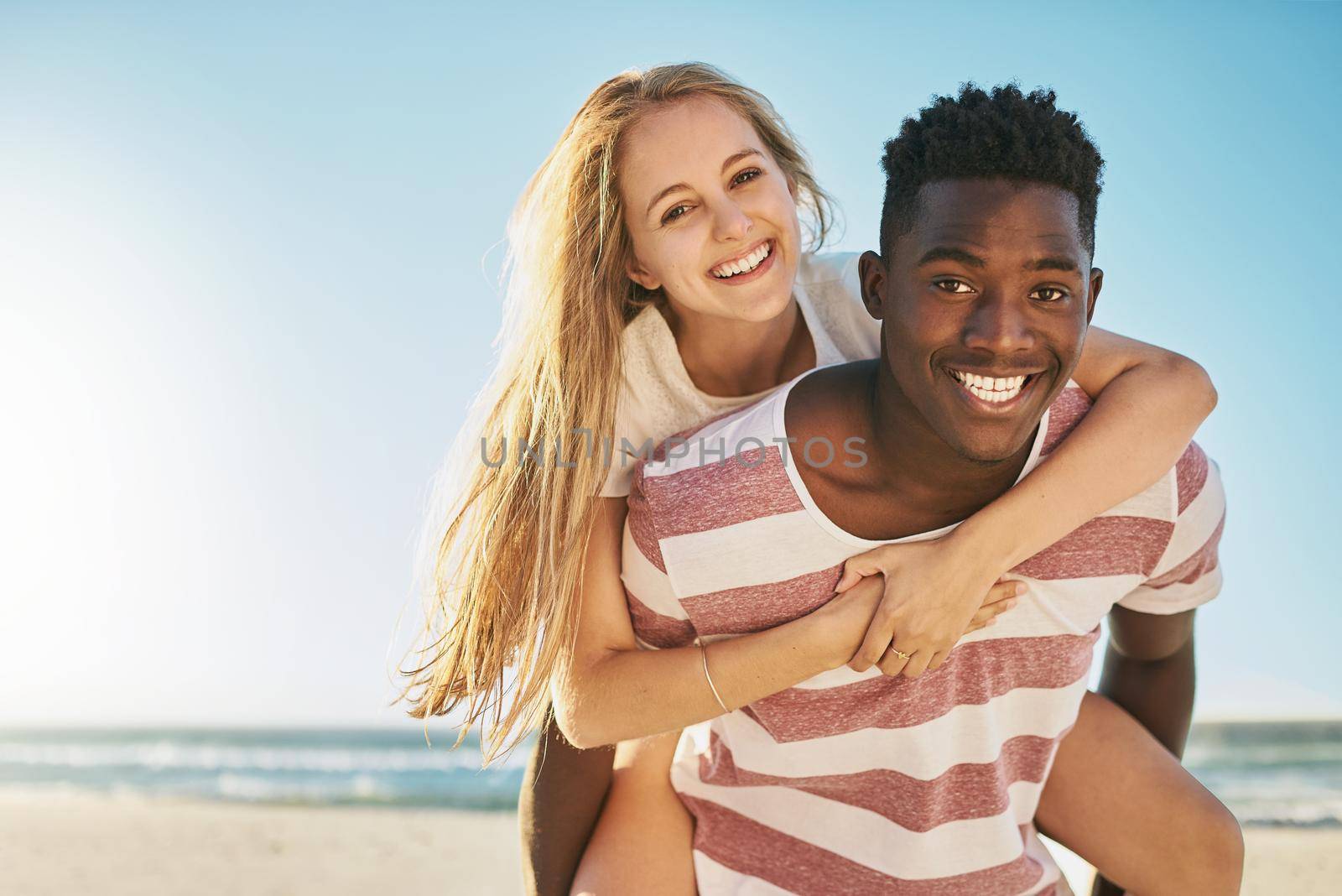 Nothing says summer romance like a piggyback ride. a happy young couple enjoying a piggyback ride at the beach. by YuriArcurs