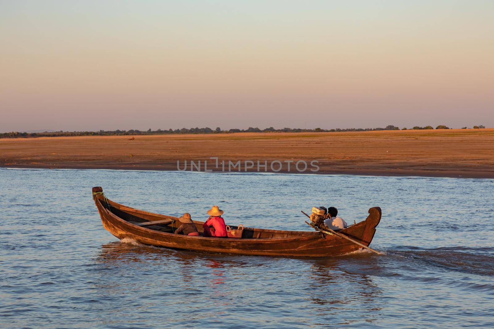 A man and two women are traveling in a wooden boat on the Irrawaddy in Myanmar