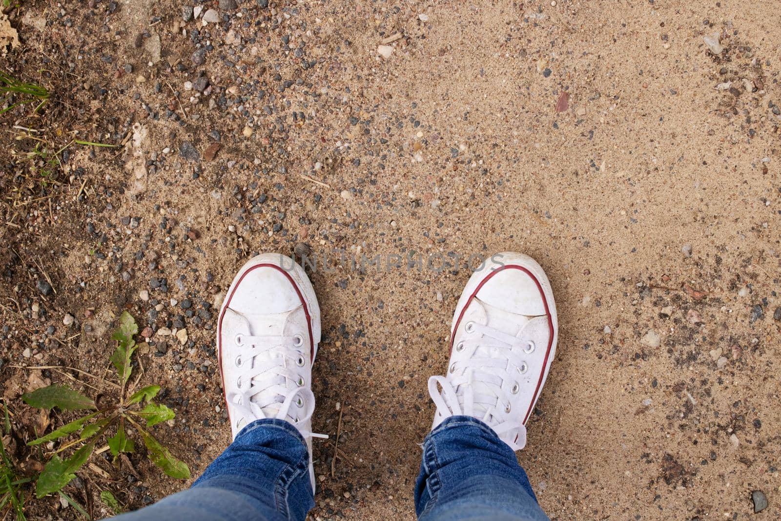 Legs in white sneakers on the sand close up