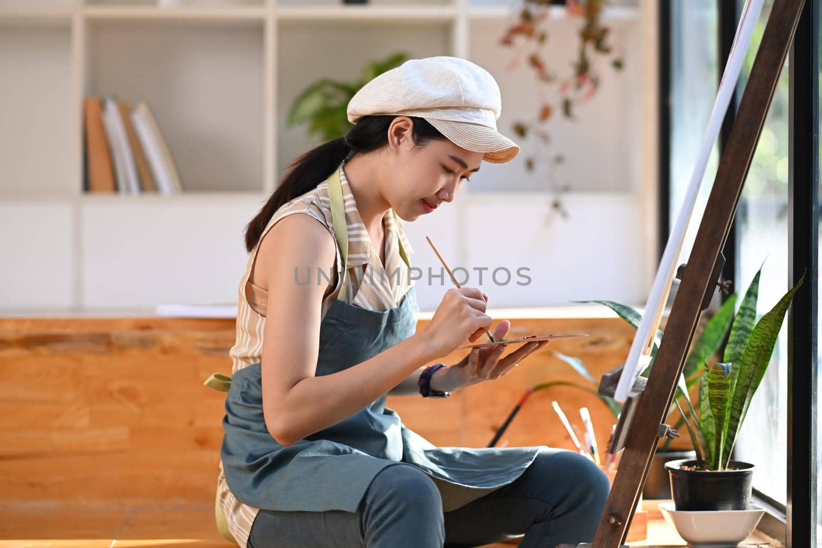 Peaceful young female artist painting picture in art studio. by prathanchorruangsak