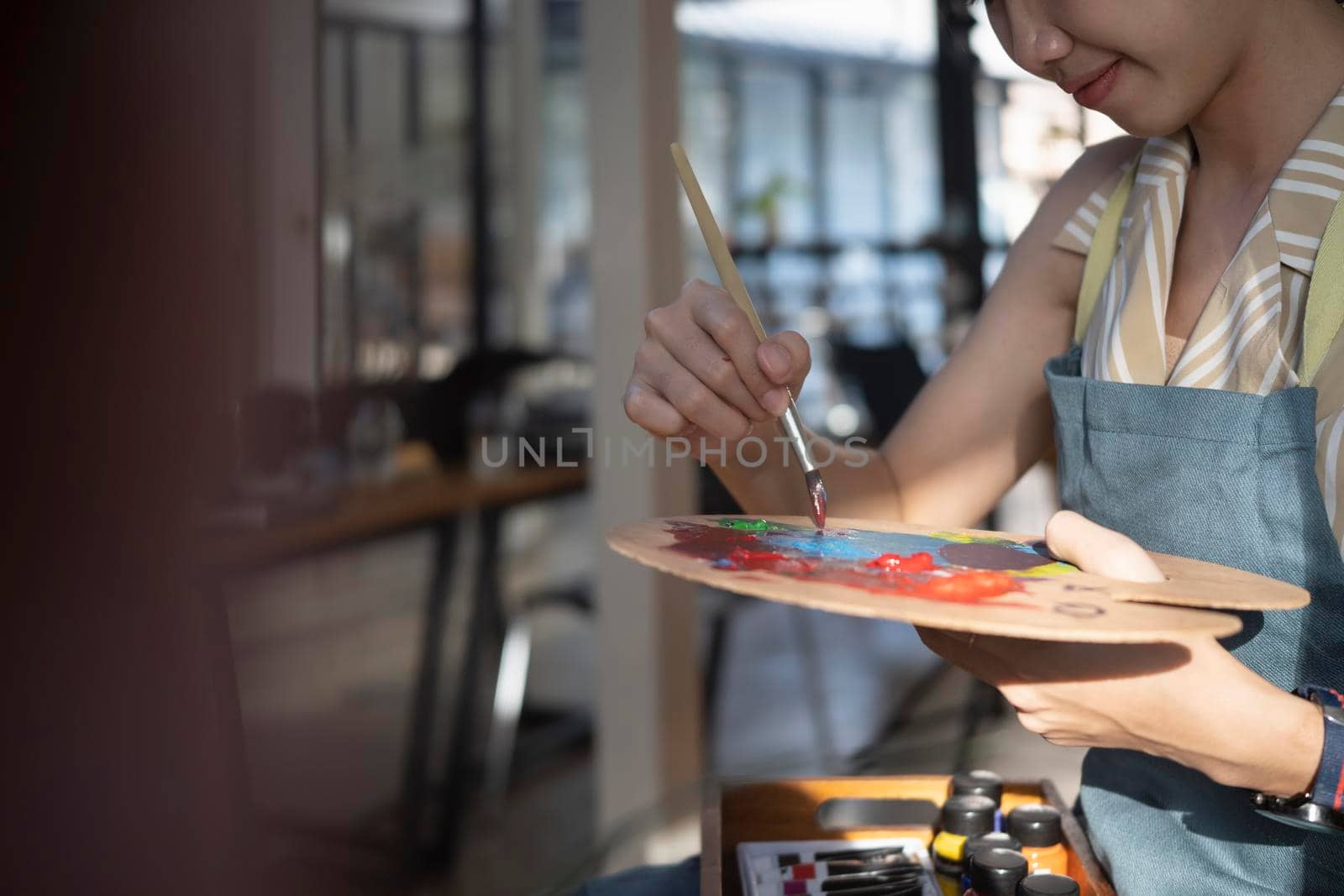 Cropped shot female artist holding a brush and mix color oil painting on palette.
