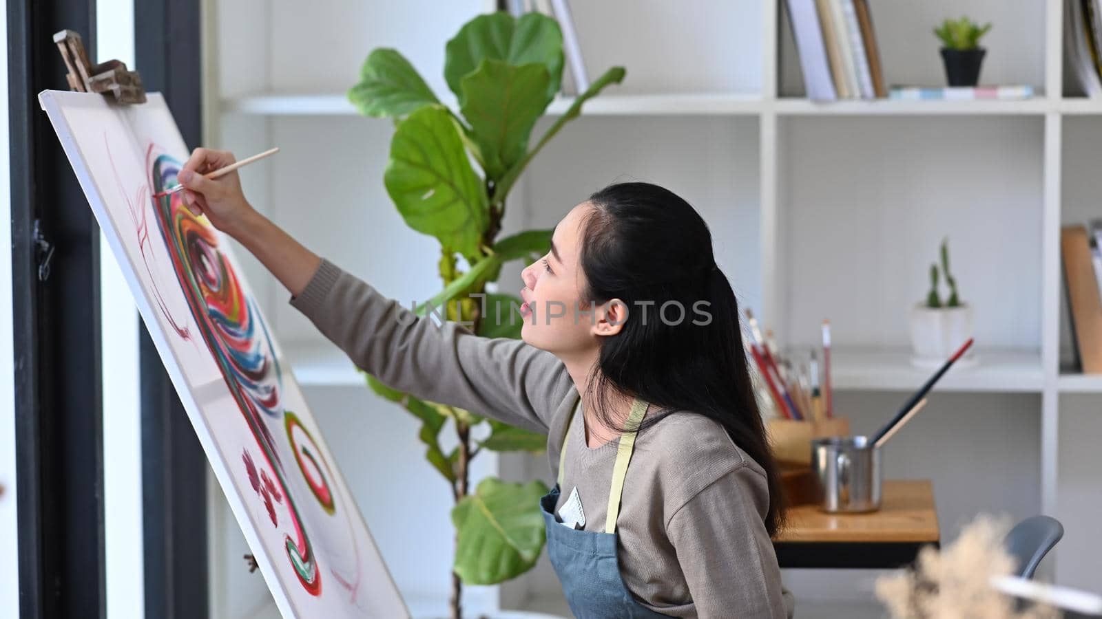 Young woman artist painting picture on easel at studio.