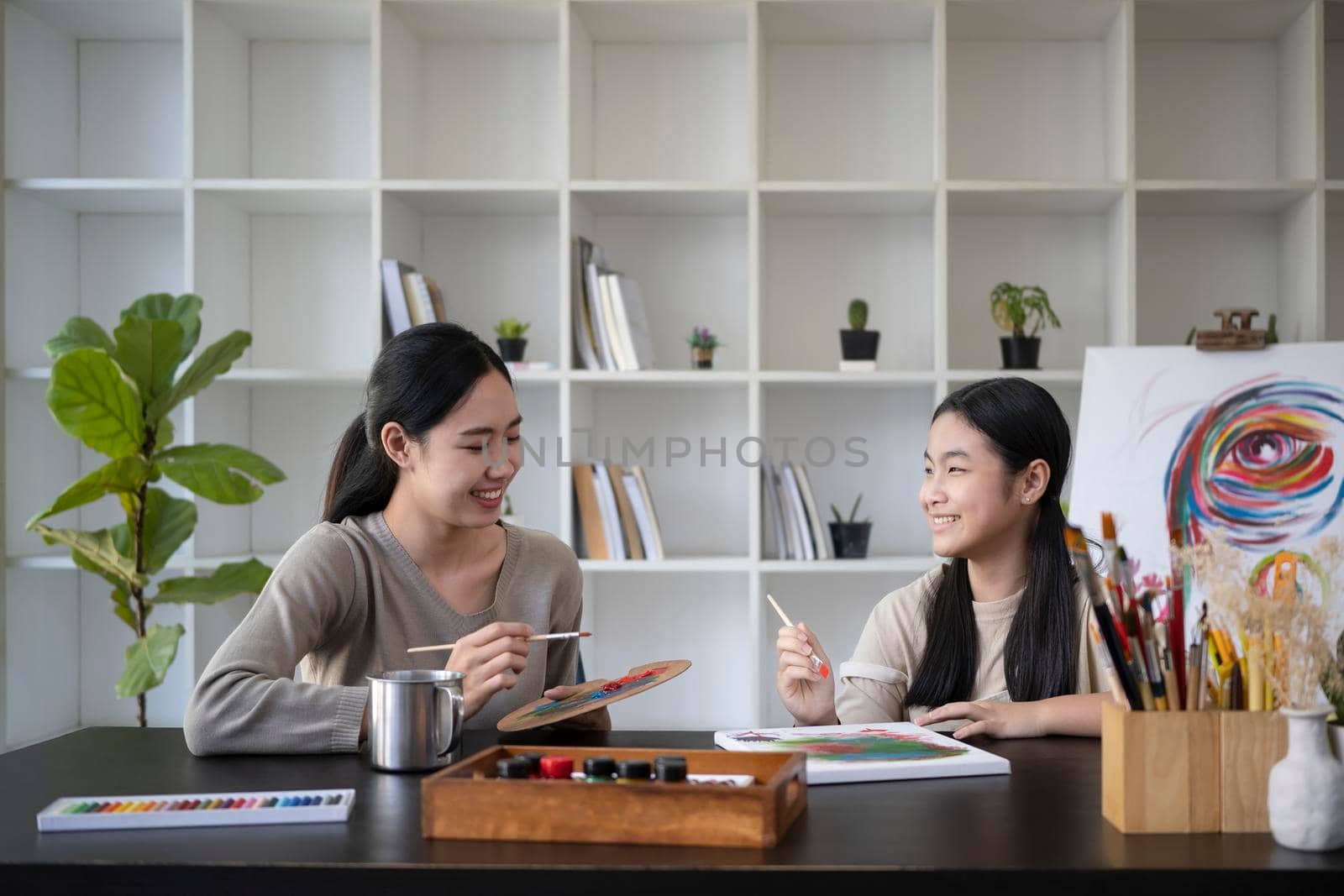 Asian mother painting picture with daughter in living room.