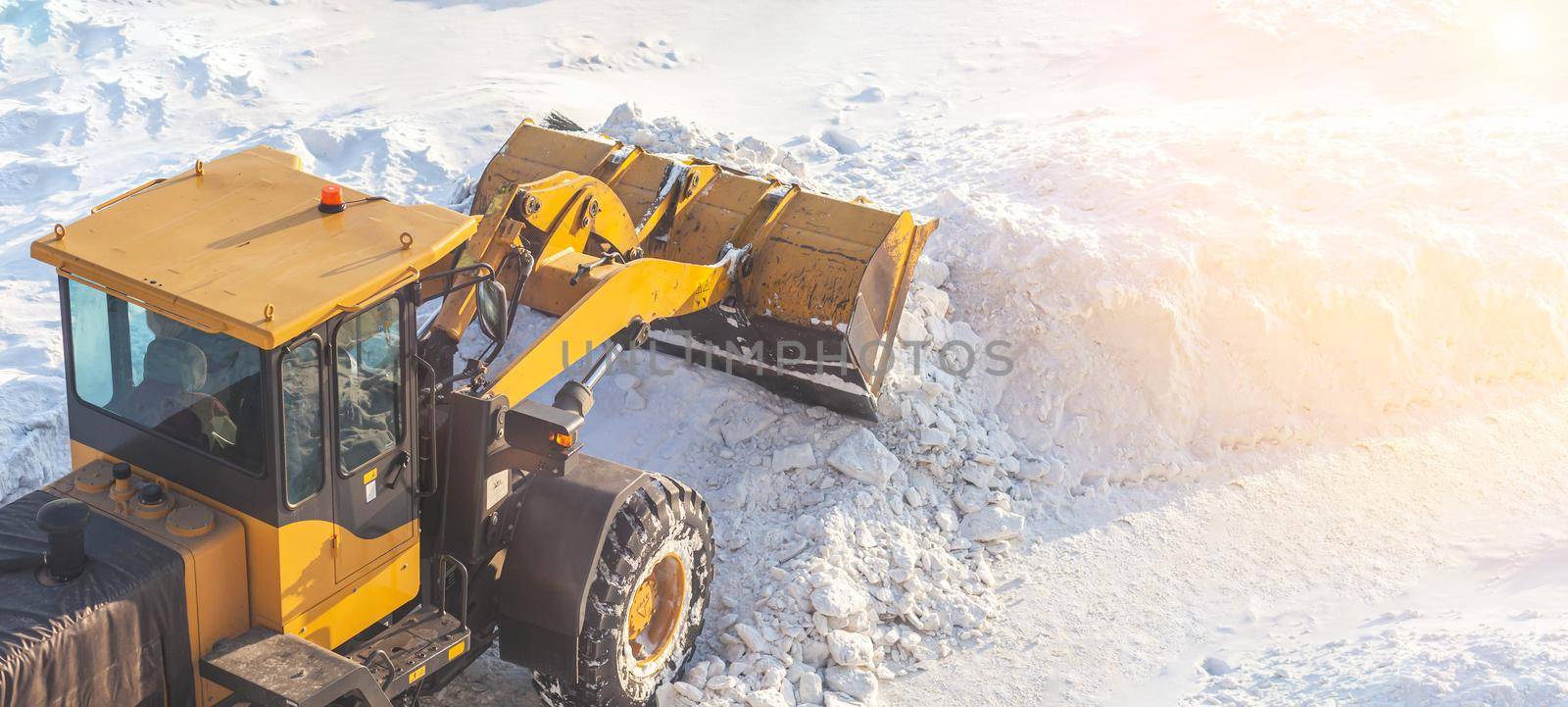 A large orange tractor removes snow from the road and clears the sidewalk. Cleaning and clearing roads in the city from snow in winter. Snow removal after snowfalls and blizzards.