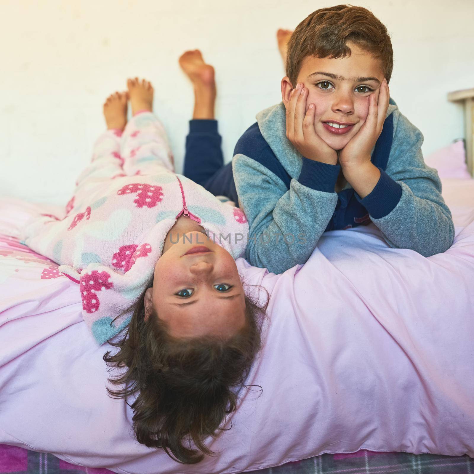 Childhood is bliss from every angle. two young siblings lying down together on a bed at home. by YuriArcurs
