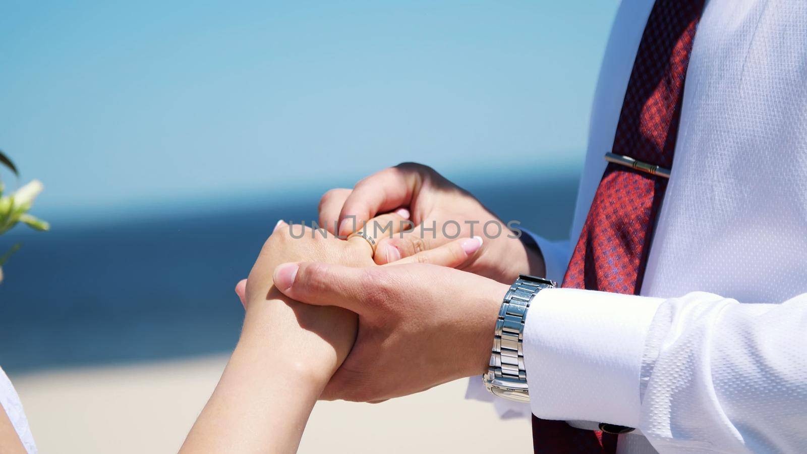 close-up, the bride and groom wear rings to each other, against the background of the sea, sand and blue sky. summer, day. High quality photo