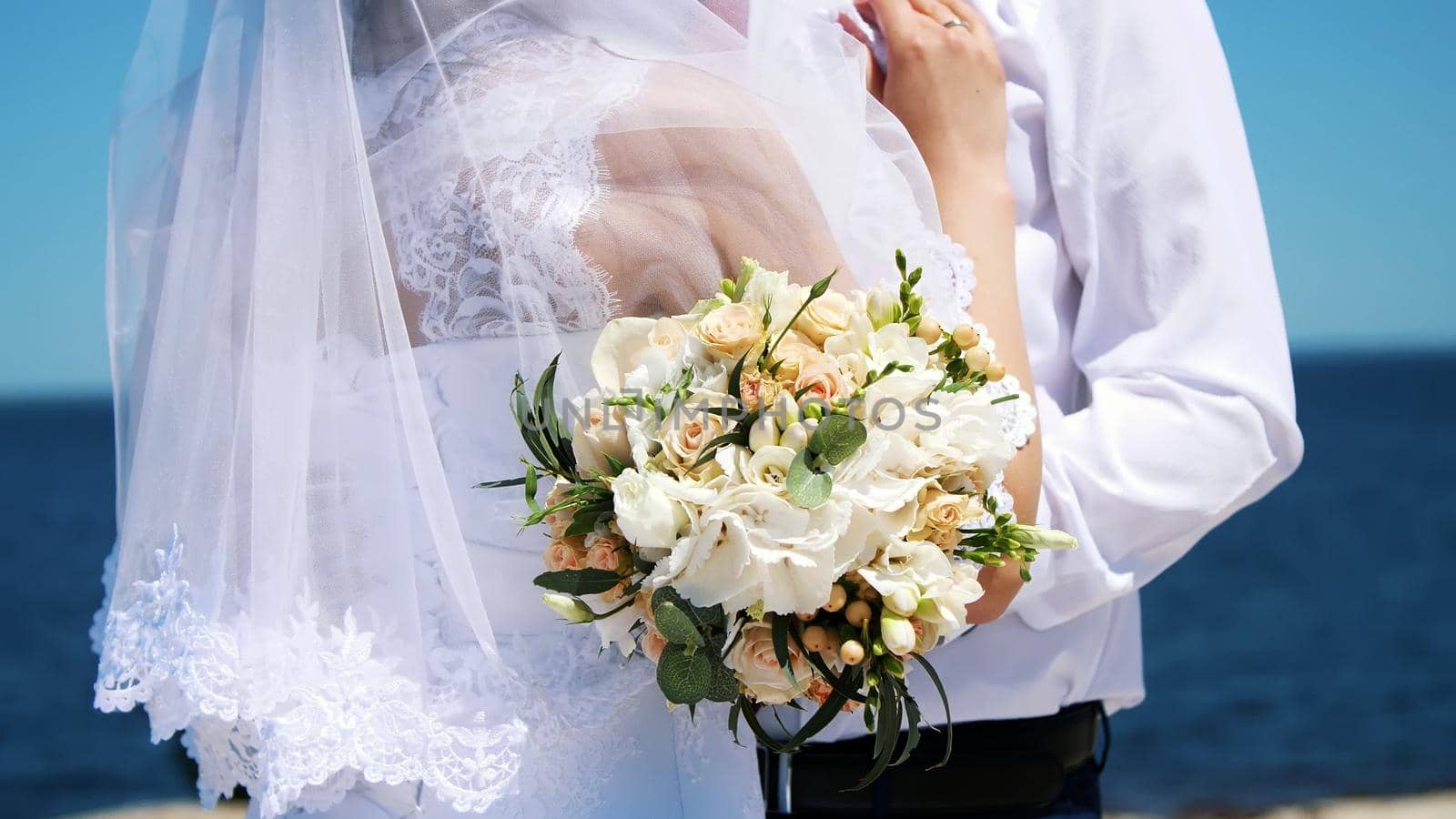 close-up of a wedding bouquet, amid hugs of newlyweds in wedding dresses. in the background sea and sky. High quality photo