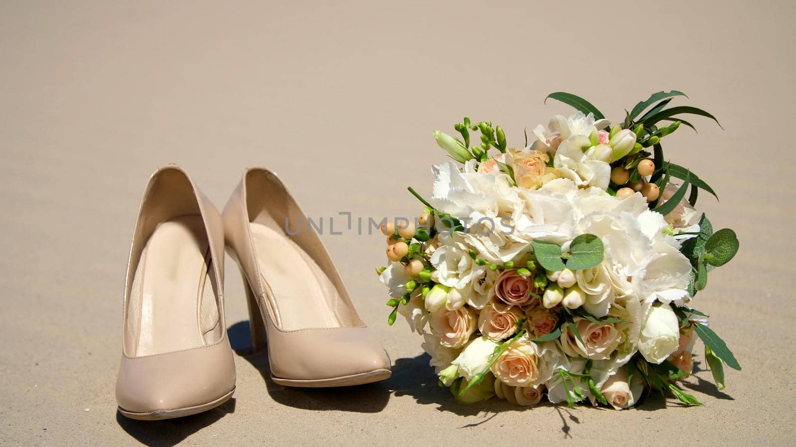 summer, desert, wedding female beige heels stand on the sand, next to the wedding bouquet. Day,. High quality photo