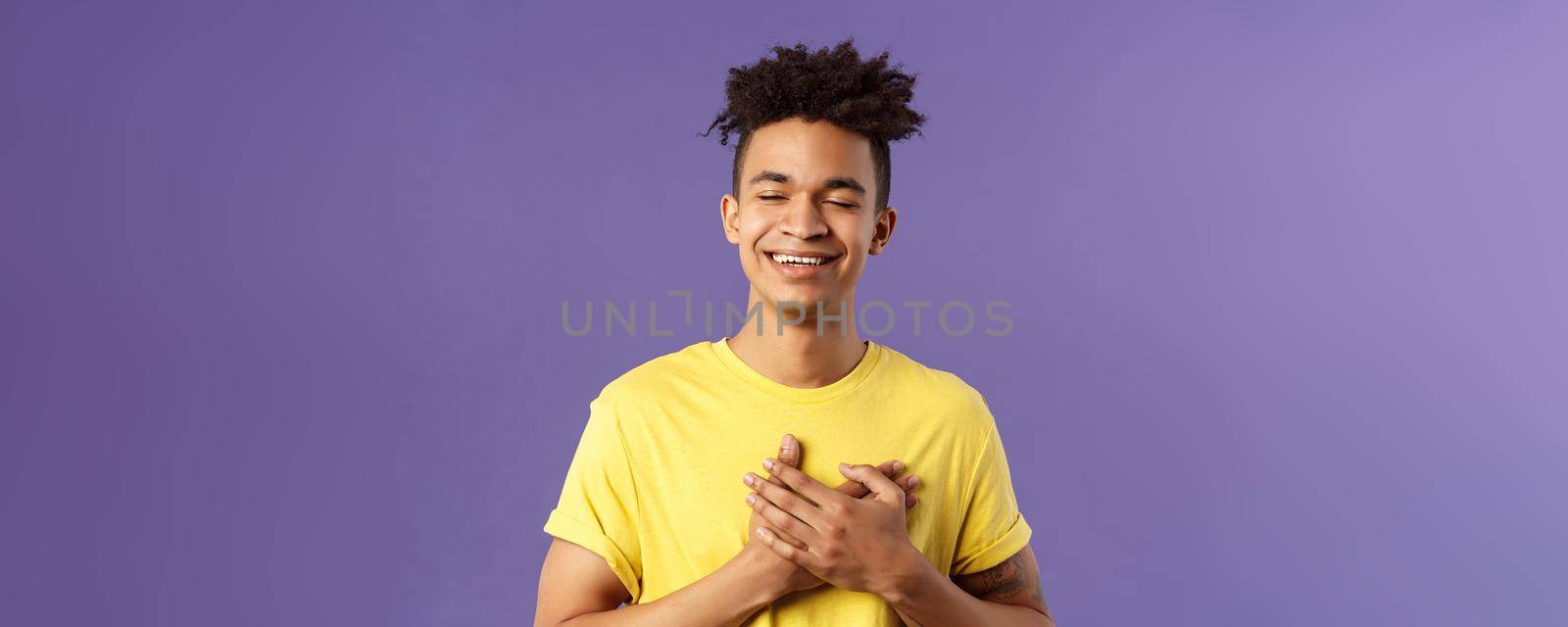 Close-up portrait of happy, upbeat young dreamy guy, remember sweet memories, hold hands on heart, smiling touched and delighted, close eyes grinning, recall romantic moment.