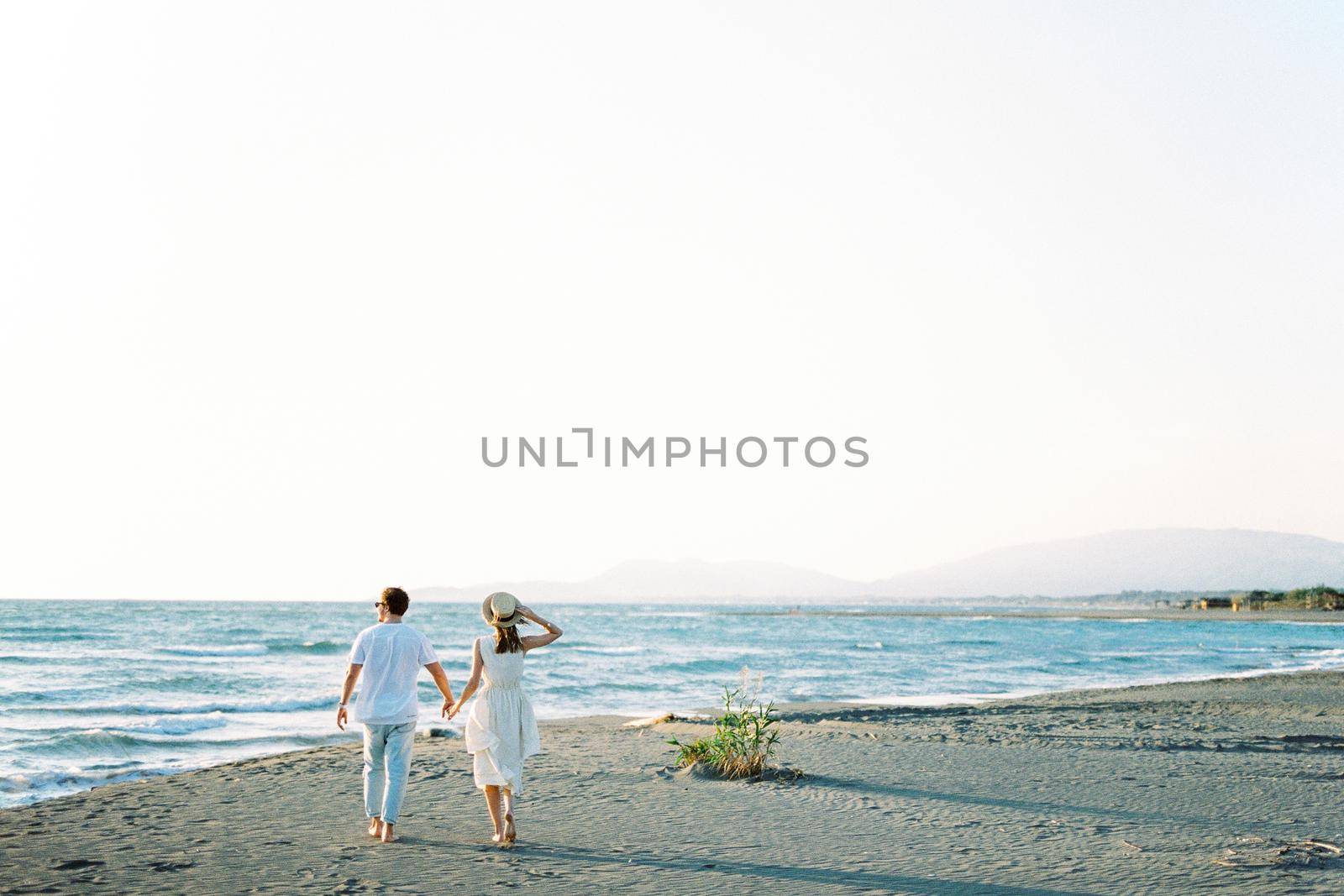 Man and woman walk holding hands on the sandy beach to the sea. Back view. High quality photo