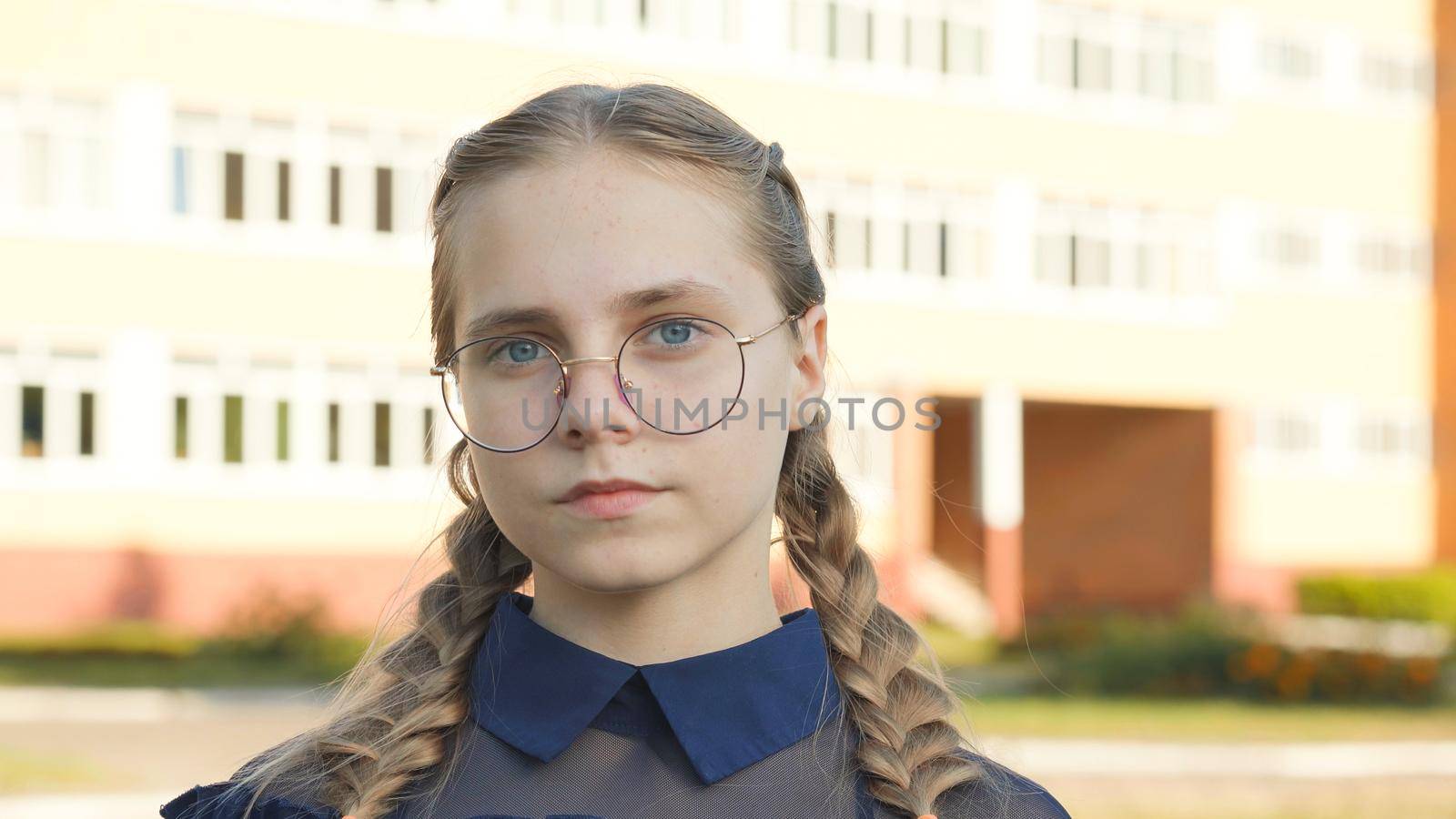 A teenage girl wearing glasses in front of a school
