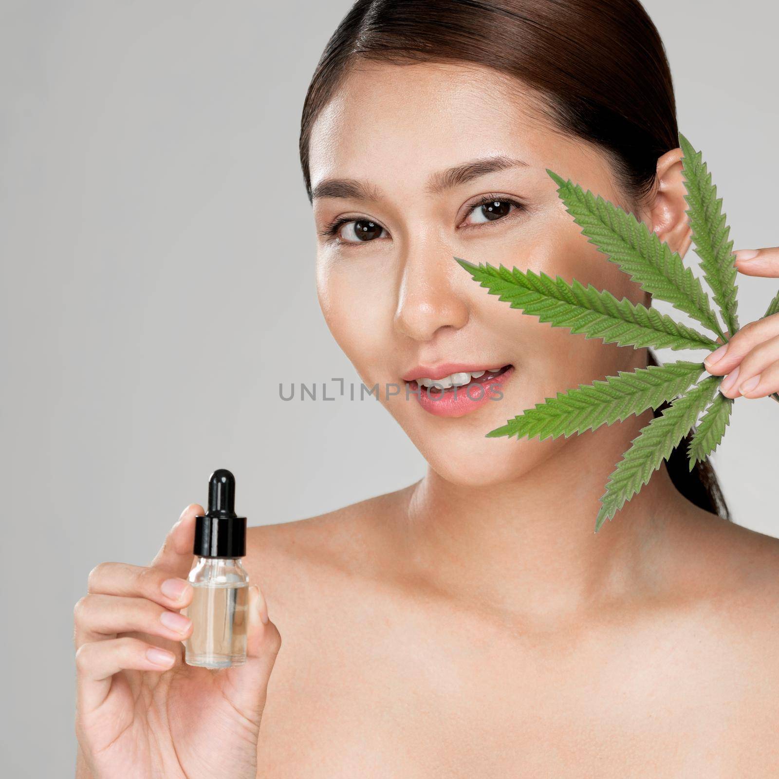 Closeup young ardent woman with healthy skin holding hemp leaf and cbd oil. by biancoblue