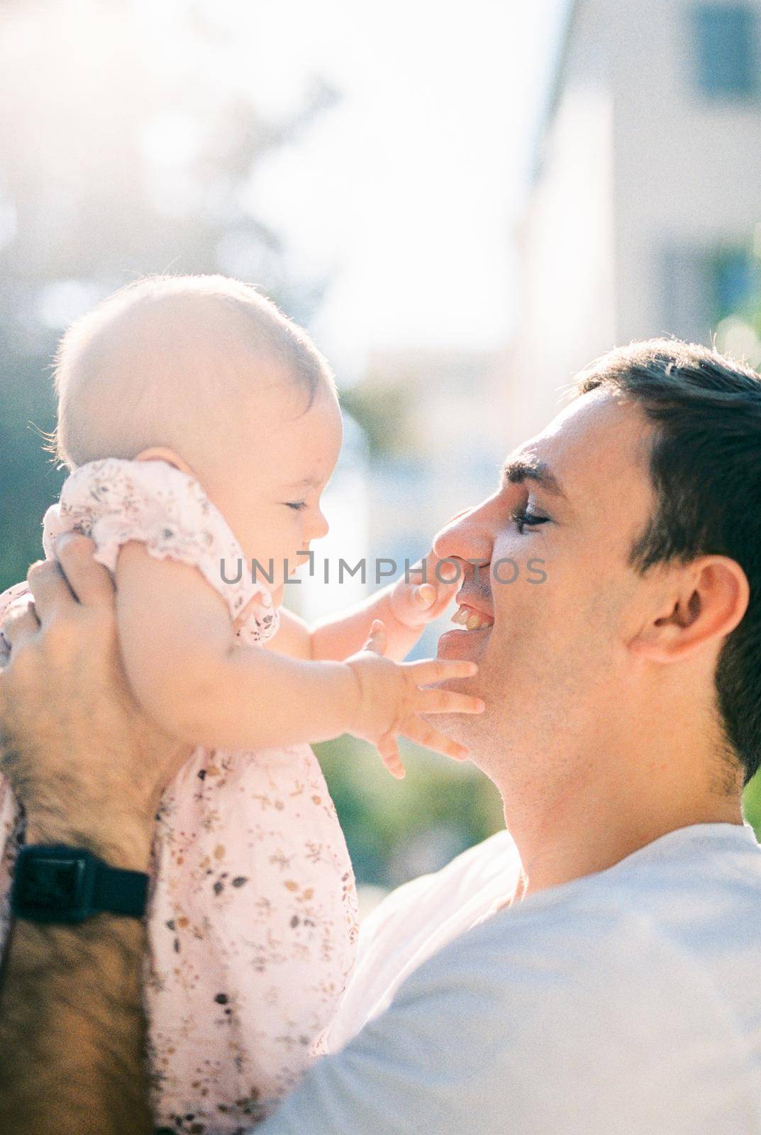 Little baby touches her dad face with her hands. Side view. High quality photo