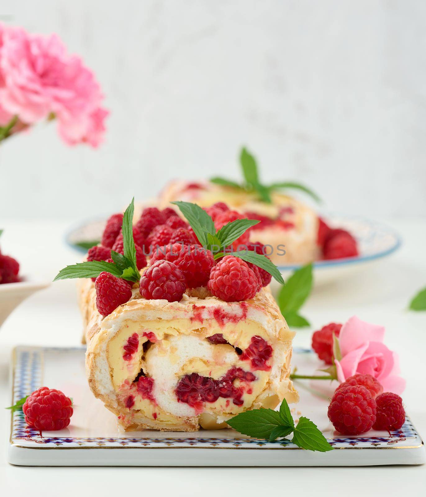 Baked meringue roll with cream and fresh red raspberry on a black wooden board, delicious dessert