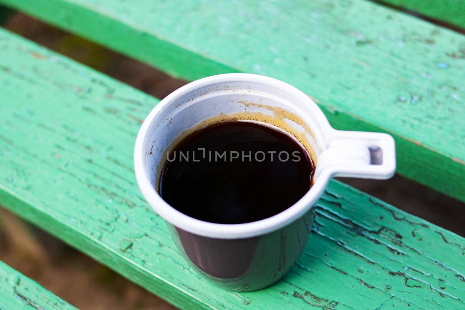 Plastic cup with coffee on a wooden bench close up