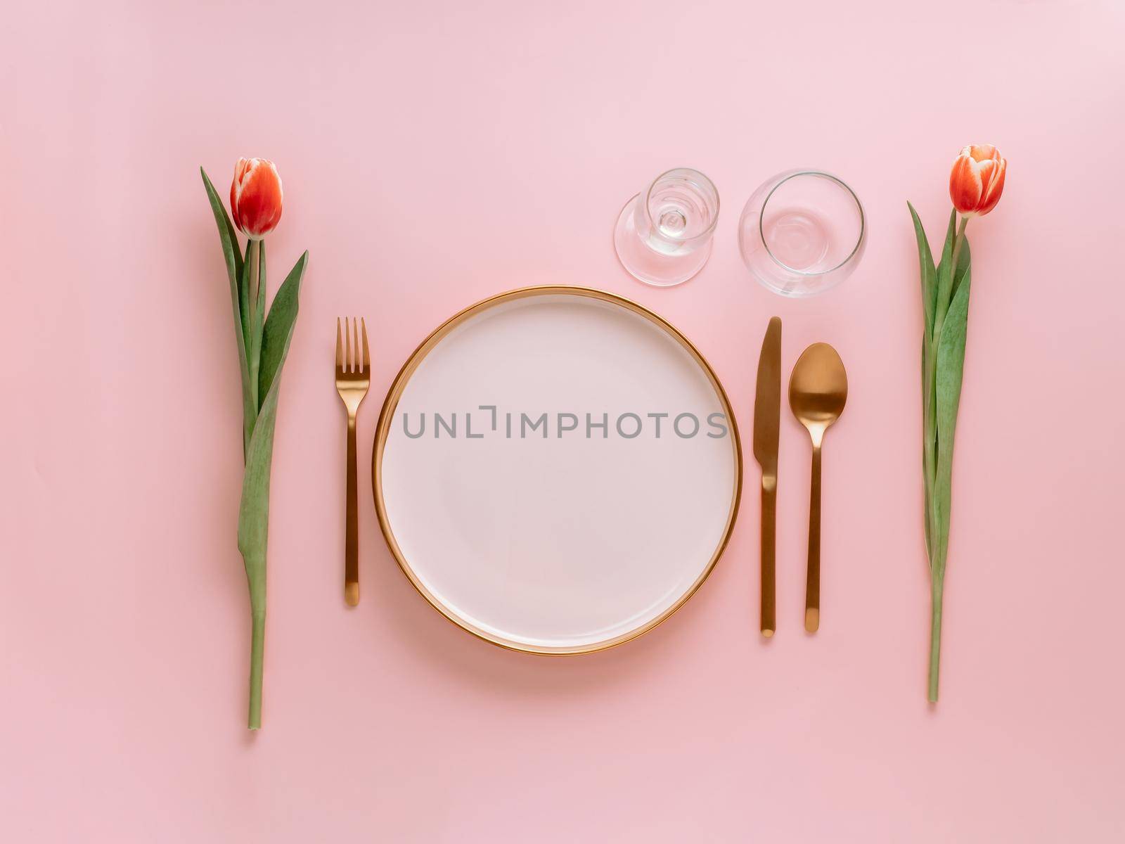 Festive pink table setting. Pink plate with gold cutlery and red tulip on pink background. Aesthetic stylish dinner table setting for Women's day, Mother's Day,wedding or anniversary.Copyspace topview