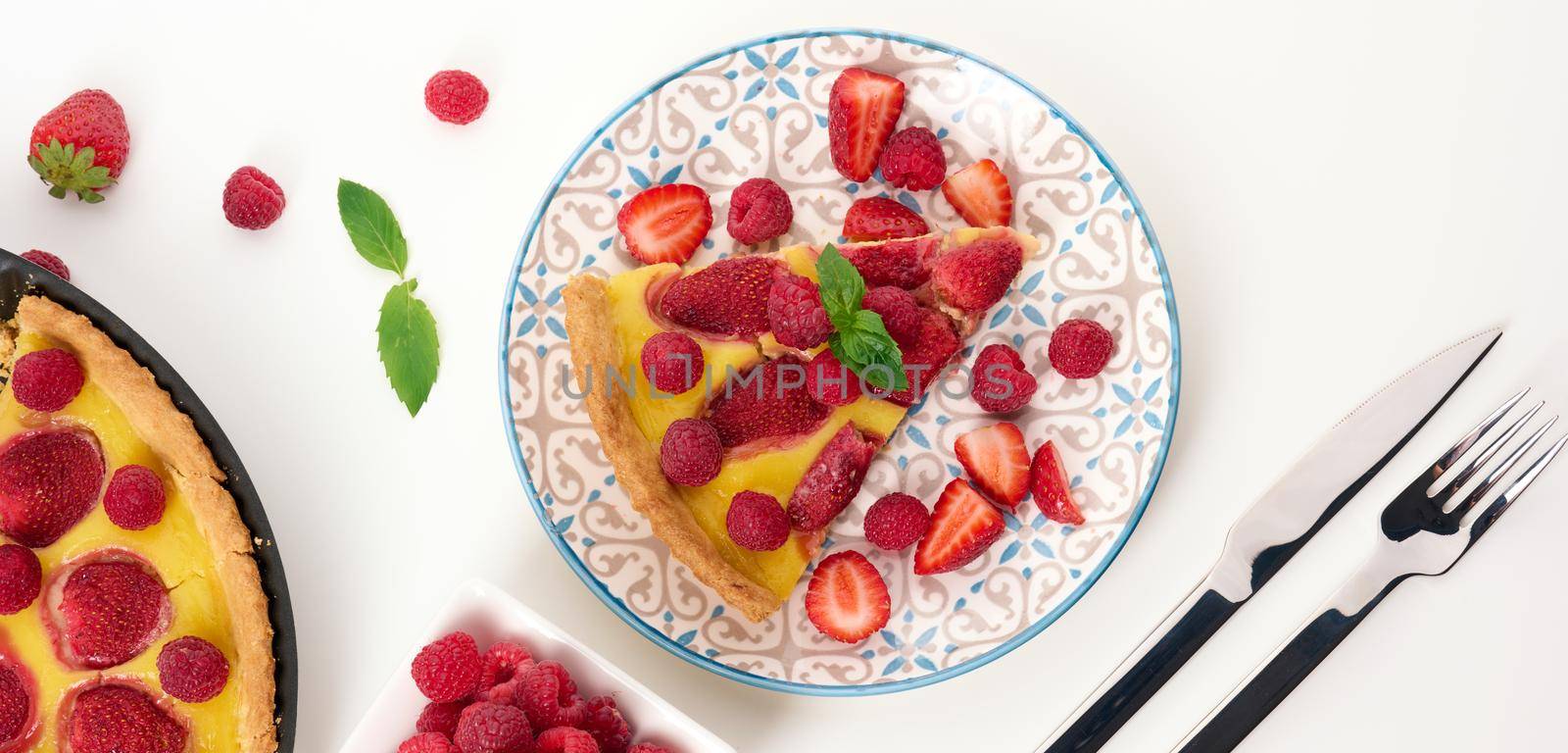 Round quiche with red strawberries and raspberries on a white table by ndanko