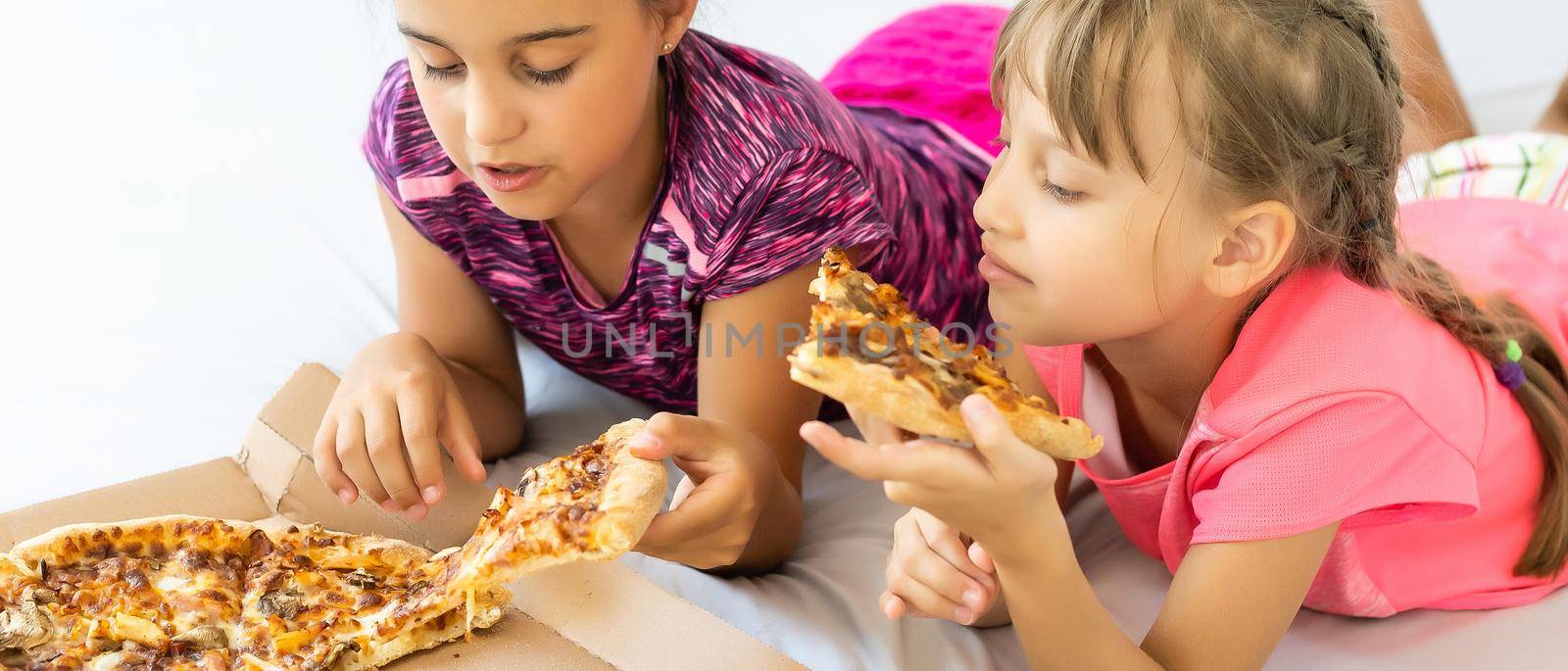 Two little girls eating pizza at home by Andelov13