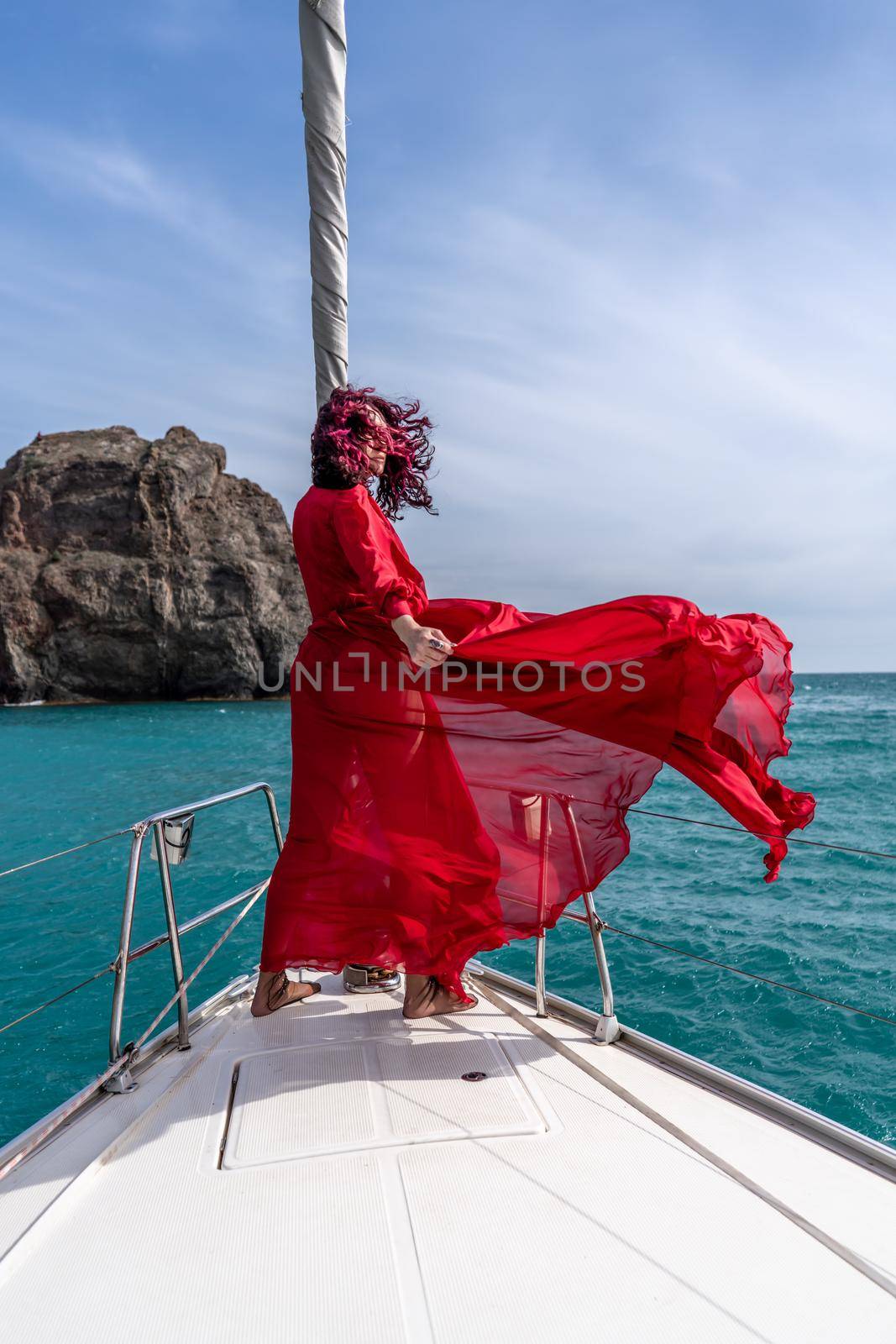 Attractive middle-aged woman in a red dress on a yacht on a summer day. Luxury summer adventure, outdoor activities