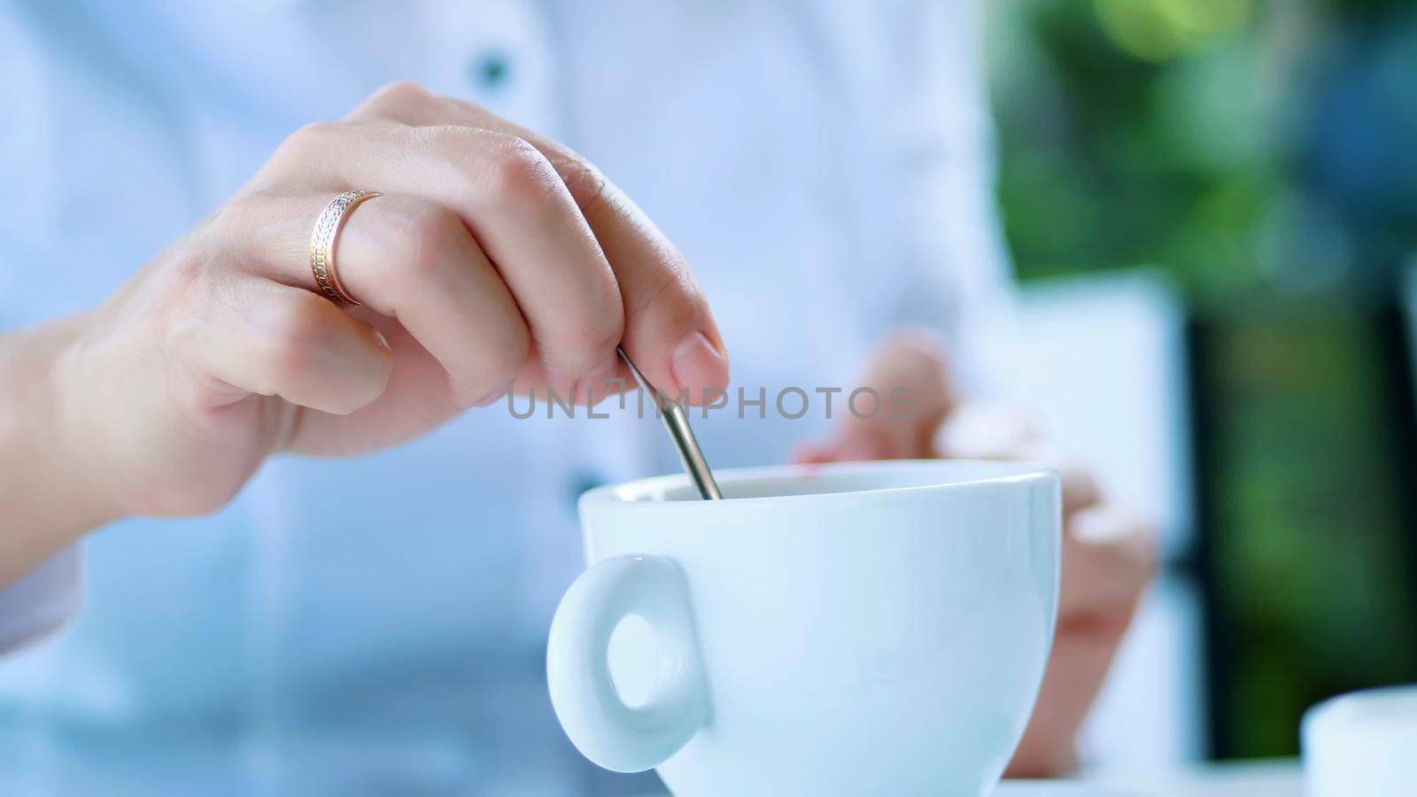 close-up, white cup with cappuccino, with thick creamy foam and marshmallows. a woman's hand slowly stirs the drink with a teaspoon. High quality photo