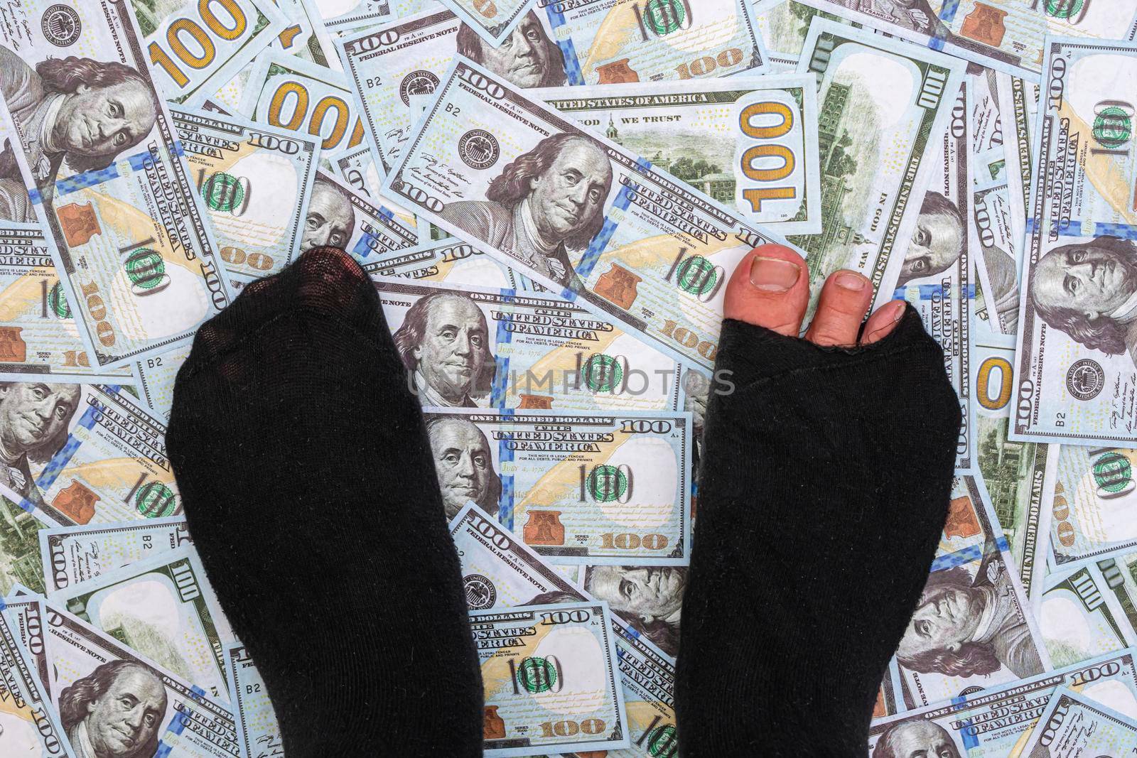 The legs of a beggar man in torn socks stand on a pile of cash
