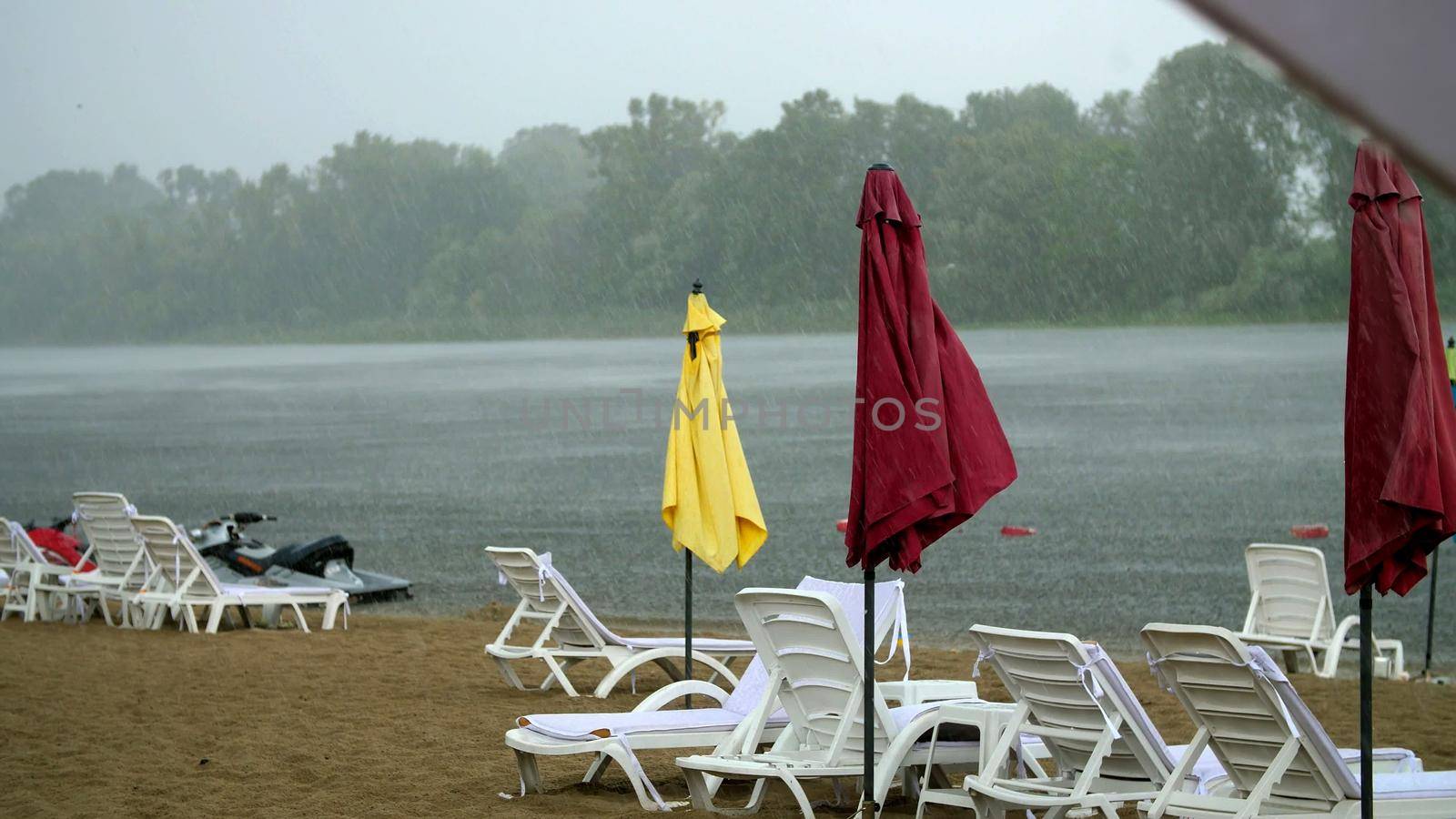 summer rain, thunderstorm, heavy rainfall on an empty beach, by river. lonely empty sun loungers and beach umbrellas are standing, strong, gusty wind,. High quality photo