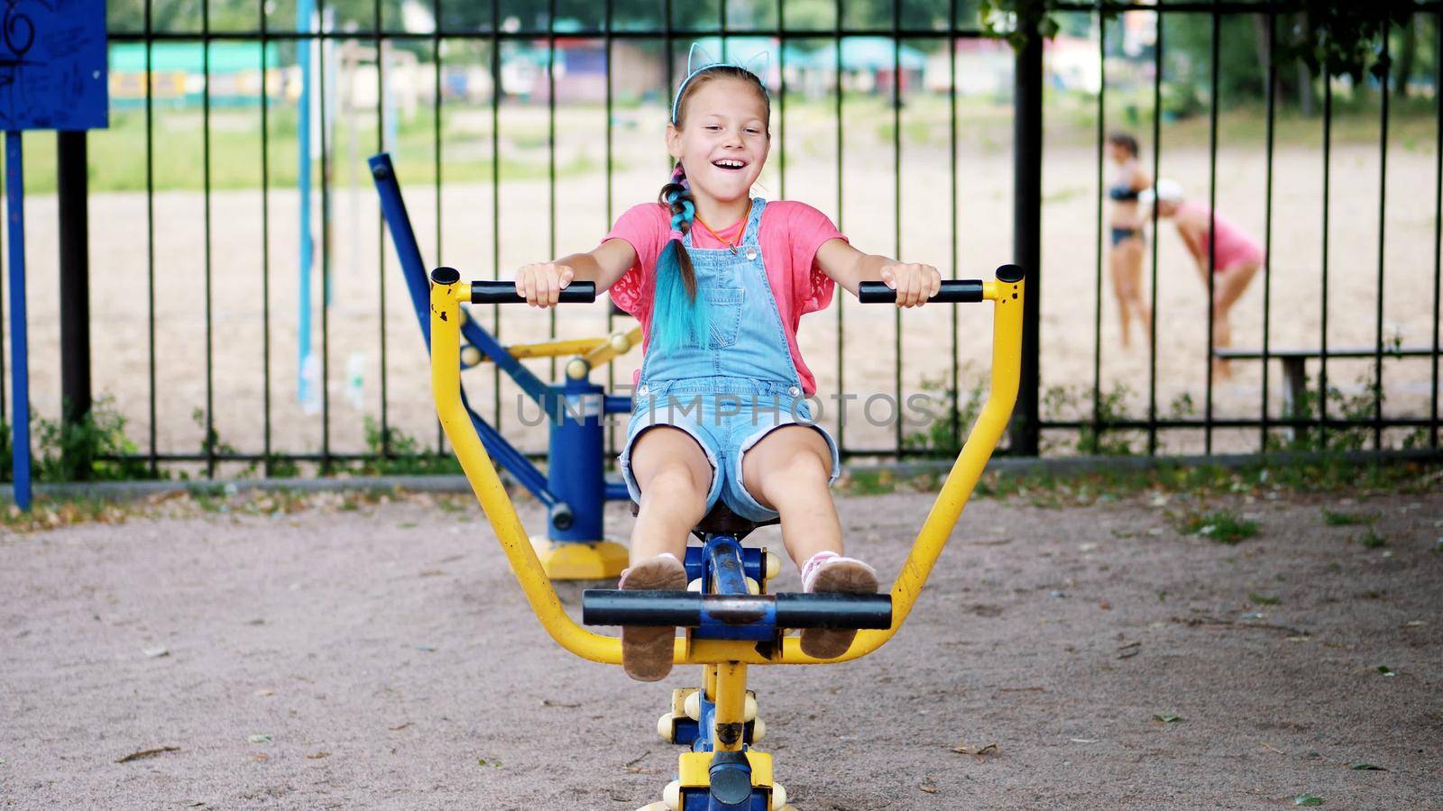 smiling, happy eight year old girl engaged, doing exercises on outdoor exercise equipment, outdoors, in the park, summer, hot day during the holidays. High quality photo