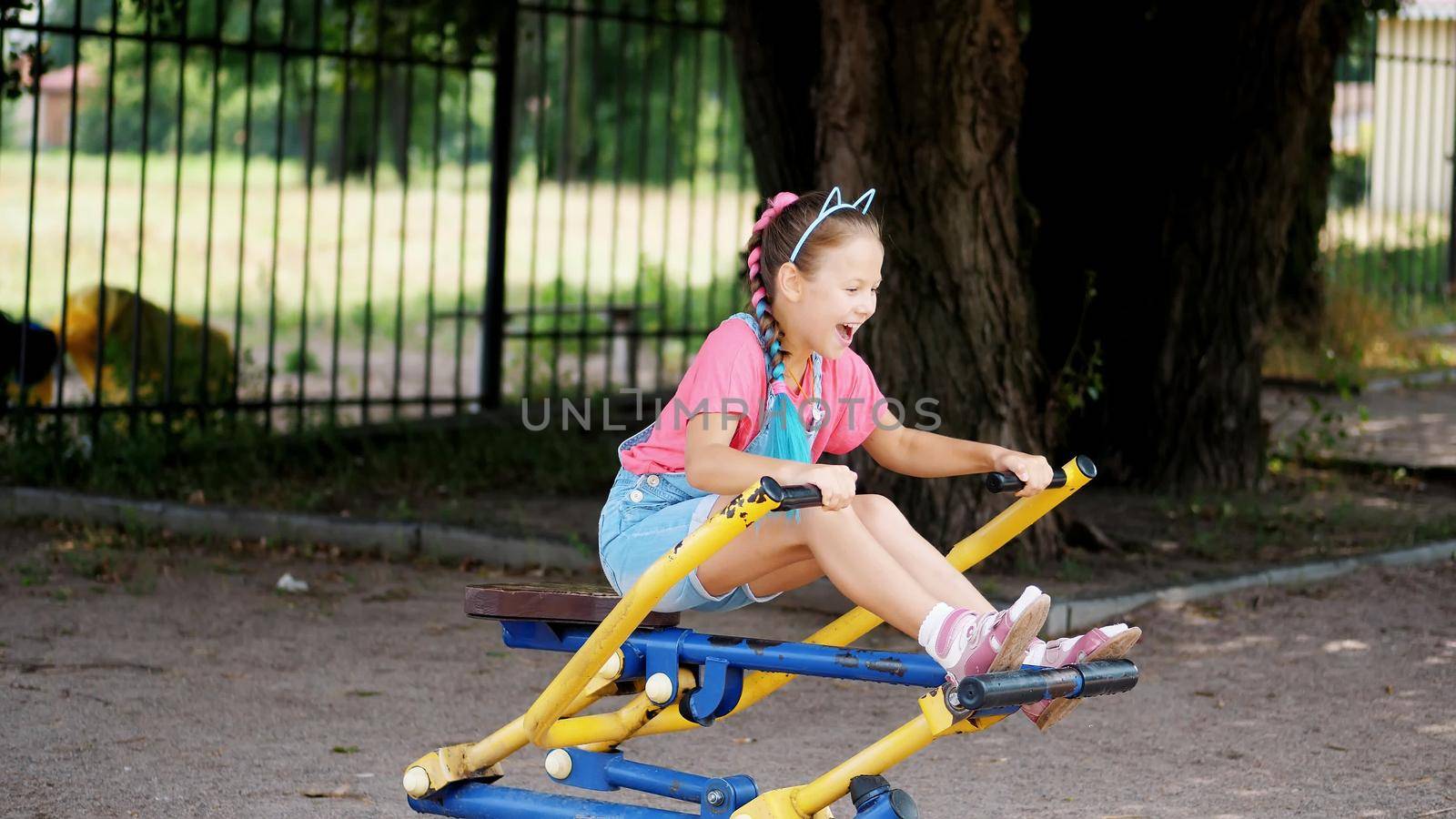 smiling, happy eight year old girl engaged, doing exercises on outdoor exercise equipment, outdoors, in the park, summer, hot day during the holidays. High quality photo