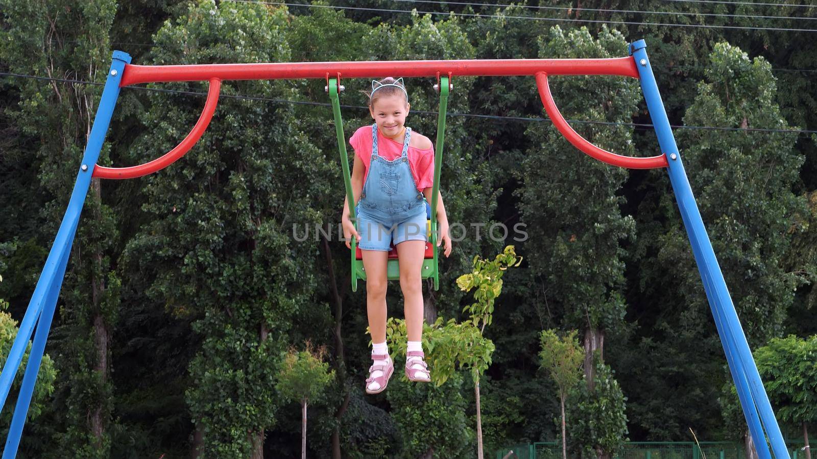 smiling, happy eight year old girl swinging on a swing, outdoors, in a park, summer, hot day during a vacation. Little girl having fun on a swing outdoor. High quality photo