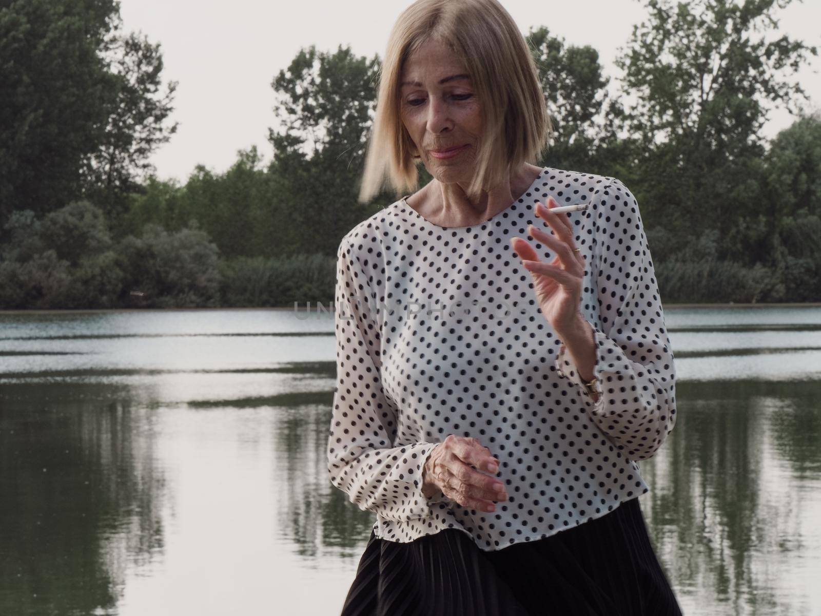 female pensioner having fun and smoking a cigarette in a park - aging free and wellness concept