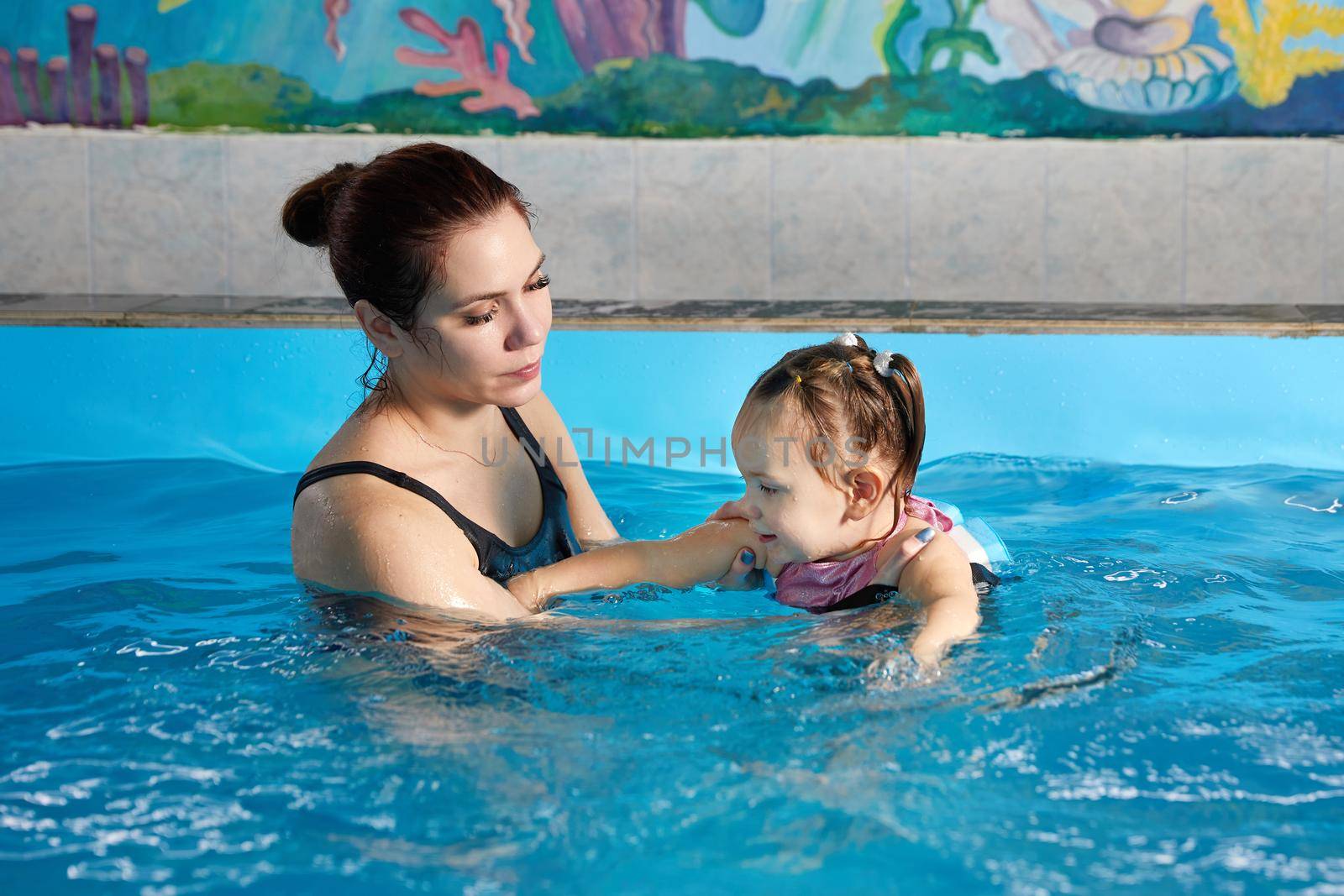 Little child learning to swim in pool with teacher by Mariakray