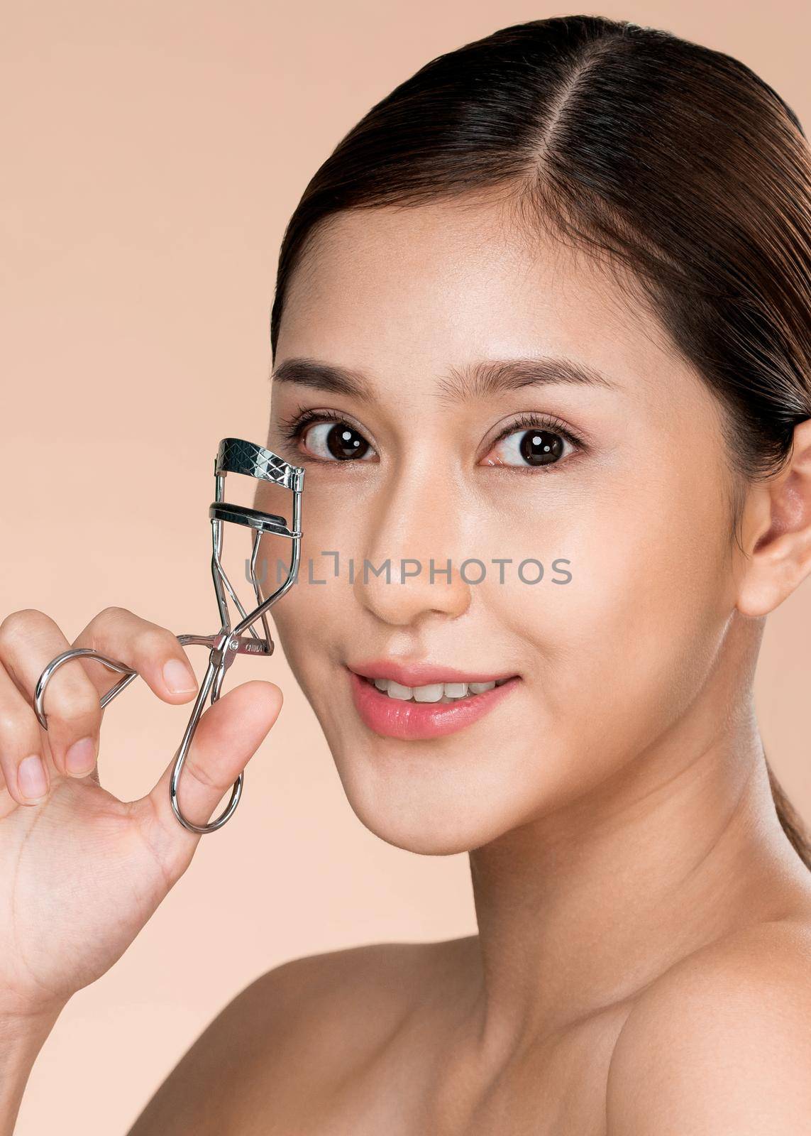 Closeup young ardent woman model with healthy flawless fair skin and soft makeup looking at camera while using eyelash curler. Beautiful girl using beauty tool on her eyelash.