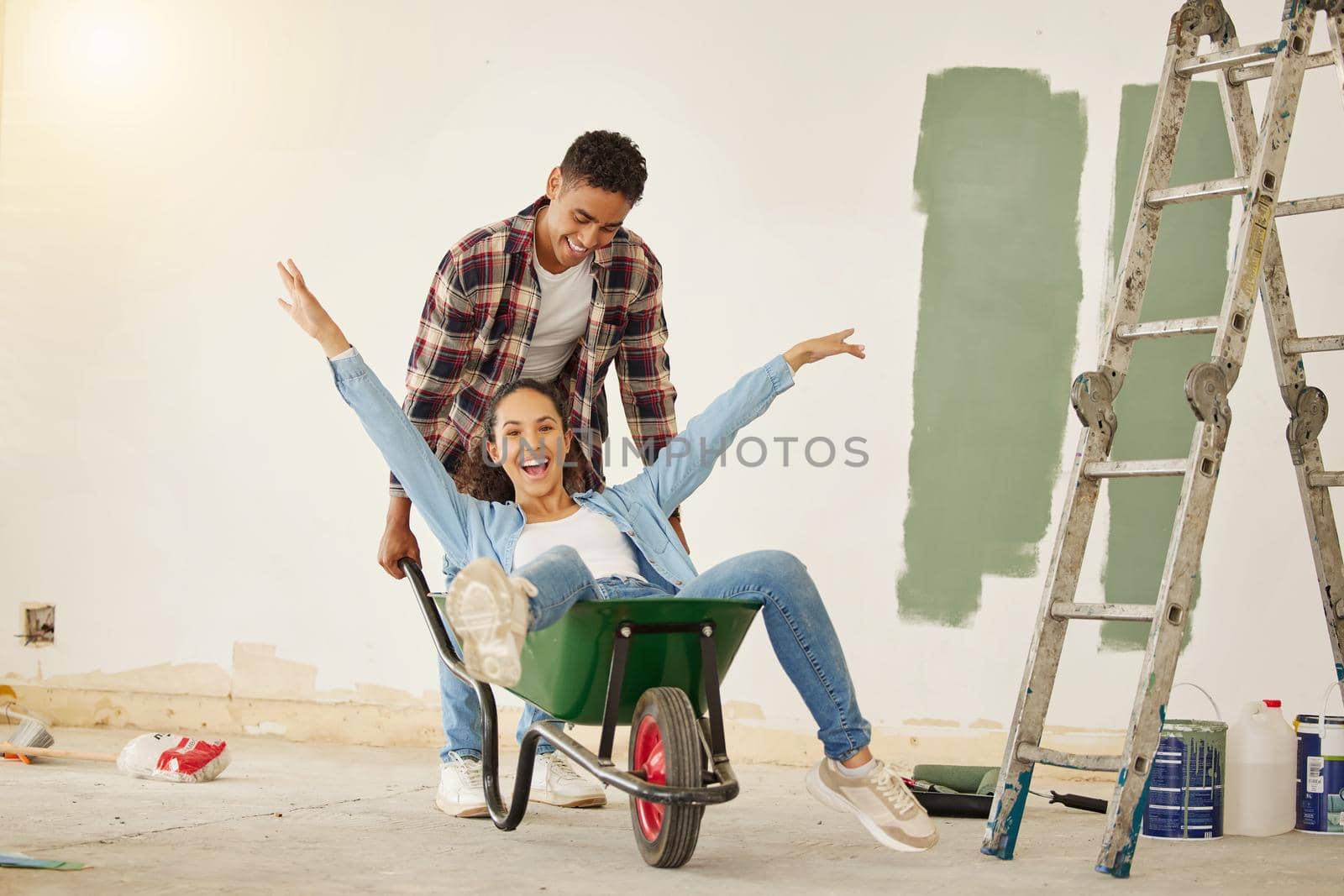 DIY, painting and happy couple smile while moving into new home, real estate property house or building. Love, creative man and woman on wheelbarrow interior design and renovation work on room wall.