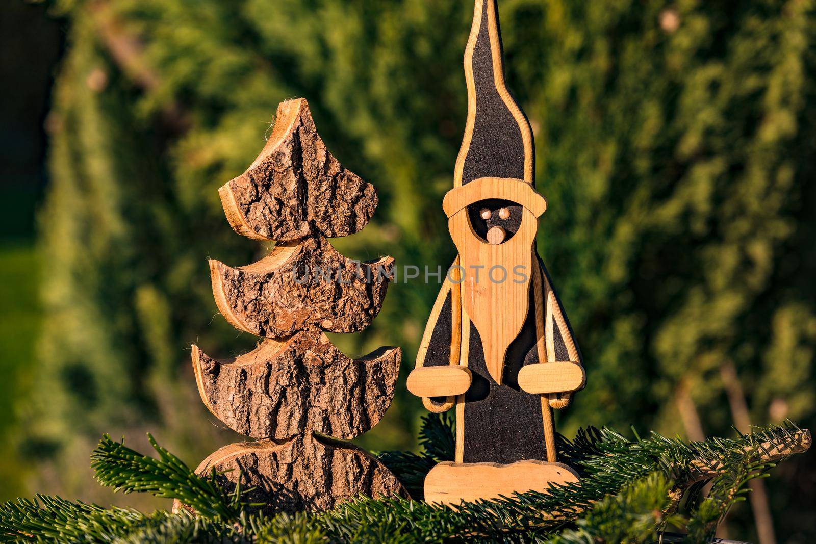 A classic wooden Santa Claus next to a wooden Christmas tree, beautifully cut out in front of a green coniferous forest