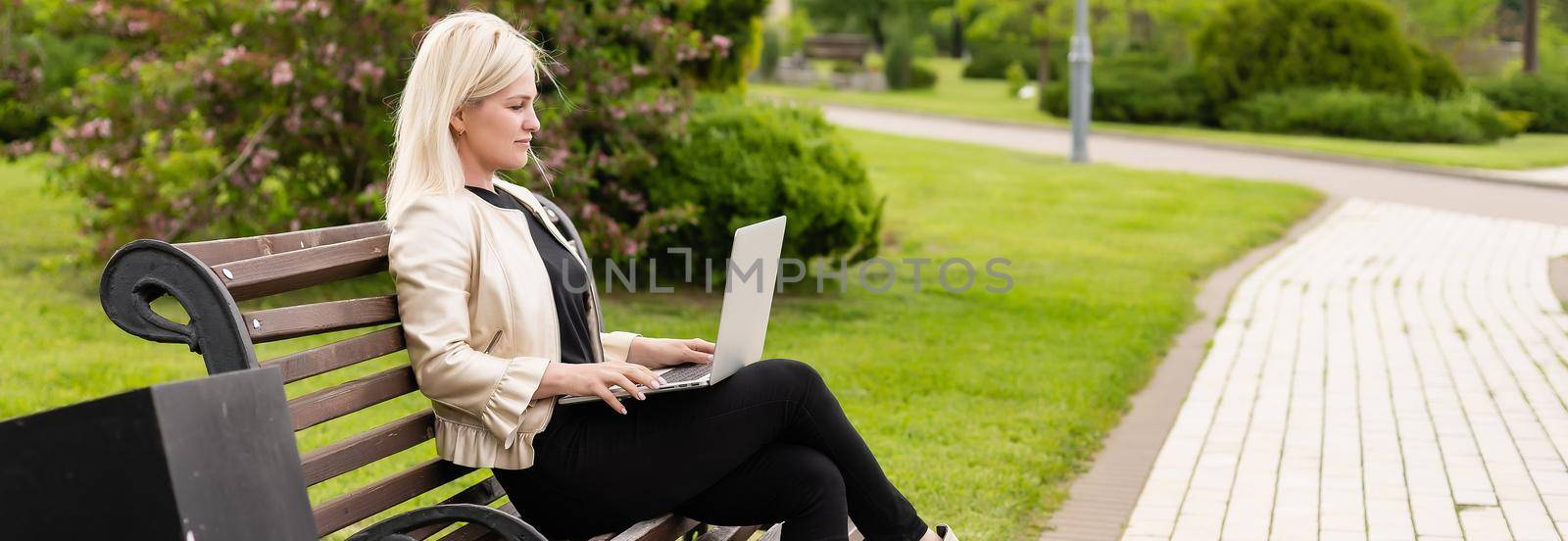 Young attractive businesswoman using a pc laptop computer while sitting on a wooden bench in a city park