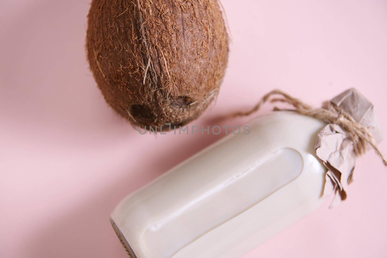 Close-up of a coconut and a bottle with healthy raw vegan organic plant based milk. Lactose and dairy free milk substitute drink, healthy eating. Flat lay. Still life. Isolated on pink background.